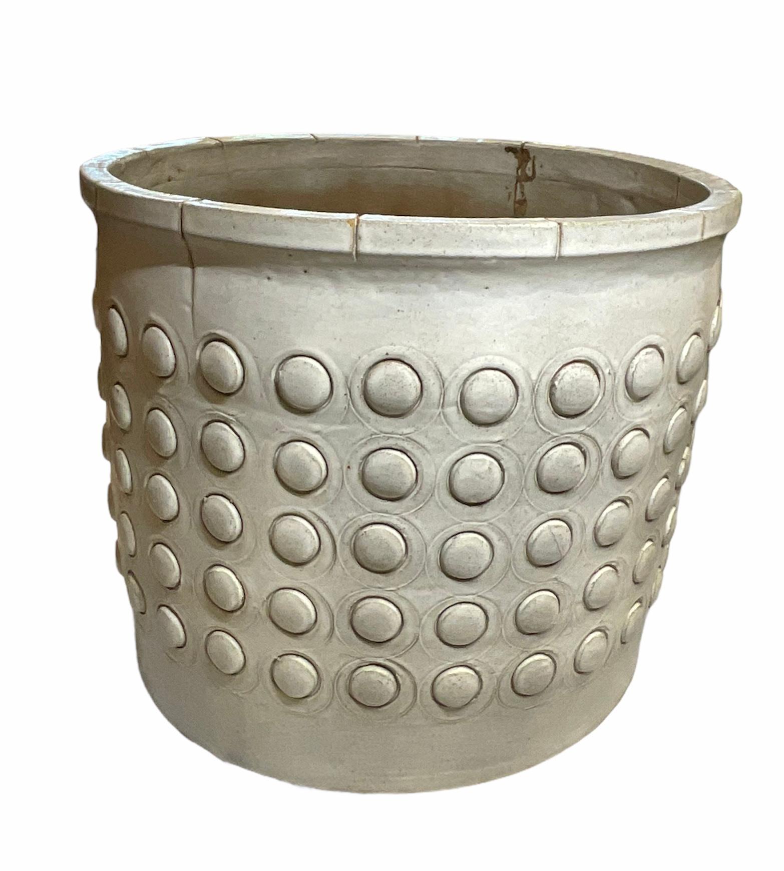 This is a Hal Lasky, Isla Del Sol Puertorican huge heavy round stoneware planter. It is painted like a light pearly color and is adorned with five rows of protruded half moon shaped spheres of the same color all around. This planter weights about