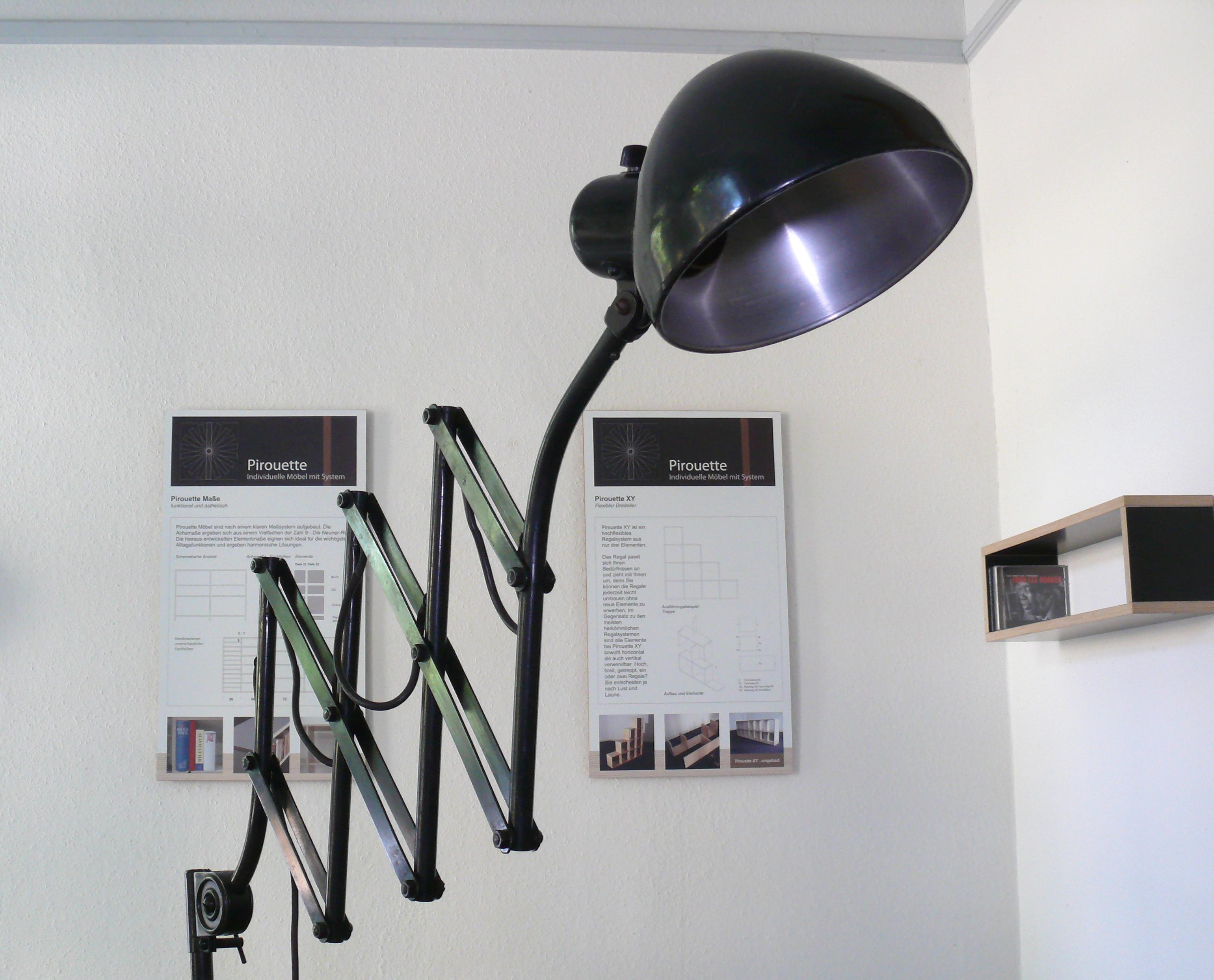 
Workshop workstation lamp from the 1930s

Manufacturer: Hala Leuchten, Zeist, Netherlands
Designer: Herman Theodoor Jan Anthoin Busquet

Black metal scissor lamp from Hala with a rotary switch on the shade and an elaborate, solid table bracket. The