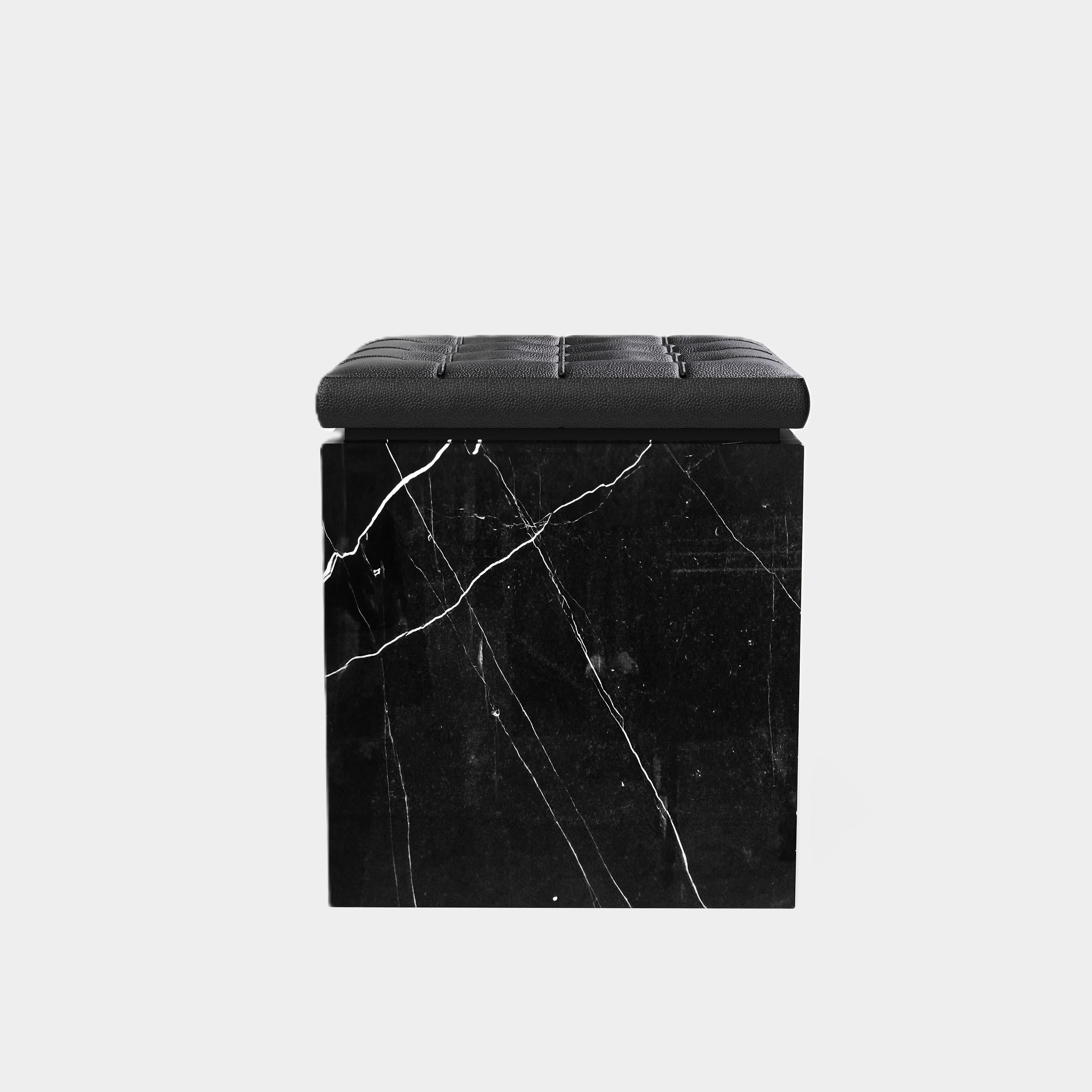 Un pouf contemporaneo con un cuscino in pelle splendidamente trapuntato su una base a zoccolo in marmo naturale di alta qualità. La parte superiore del pouf presenta un cuscino in pelle nera, con un classico disegno a ciuffi che offre una texture