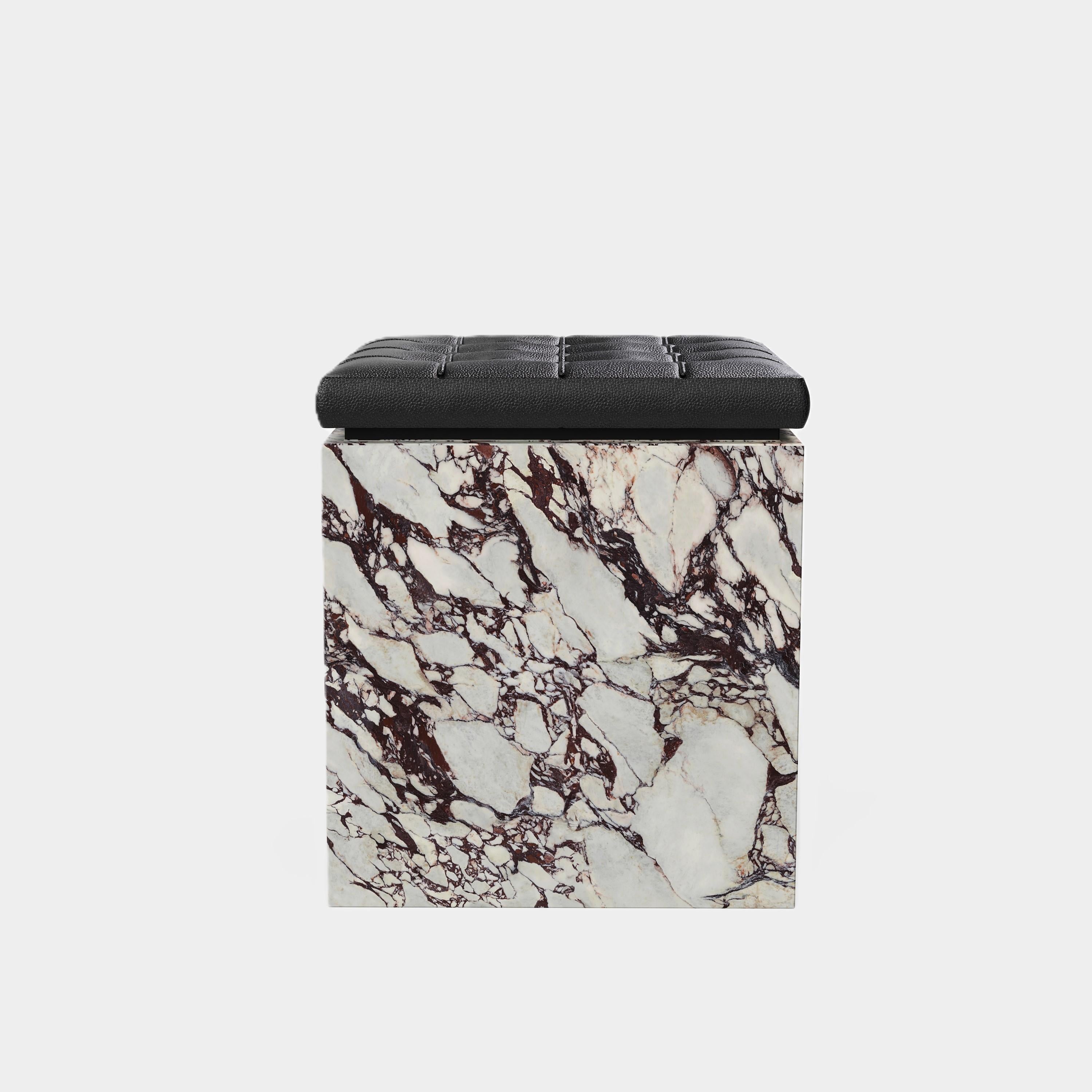 Un pouf contemporaneo con un cuscino in pelle splendidamente trapuntato su una base a zoccolo in marmo naturale di alta qualità. La parte superiore del pouf presenta un cuscino in pelle nera, con un classico disegno a ciuffi che offre una texture