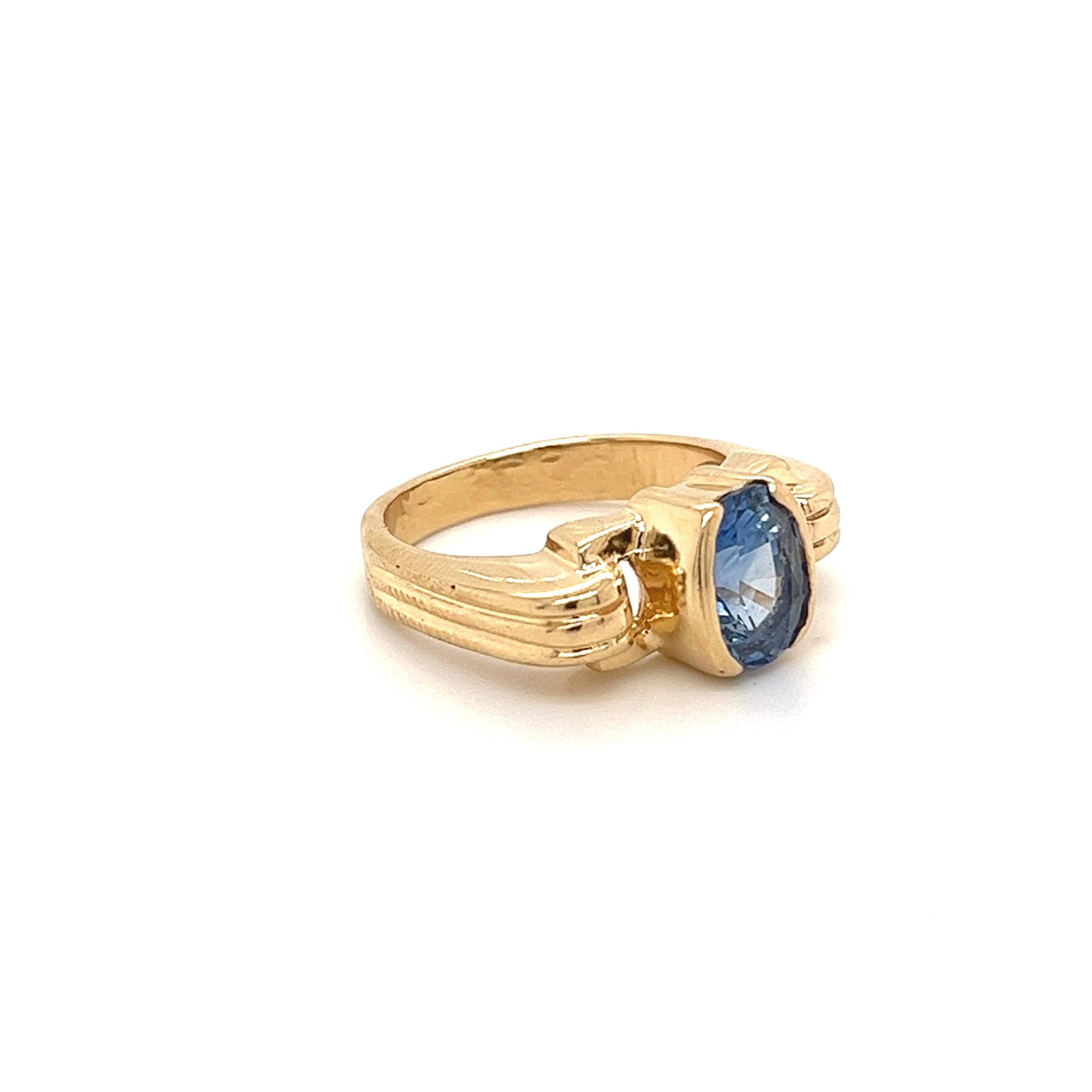 Saphir bleu de taille ovale monté dans une monture en or jaune à demi- lunette. La pierre centrale, le saphir, présente un excellent lustre et une teinte bleu profond et vibrante. La monture de la bague d'inspiration art déco est réalisée en or