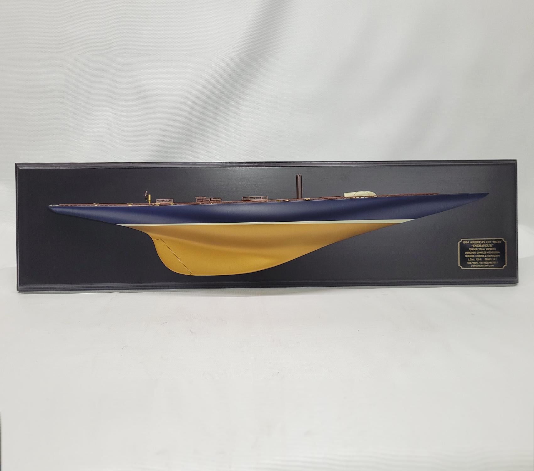 Half model of the America’s cup Yacht Endeavor. This is a 3-foot hull mounted blackboard. The hull is painted blue over gold. The planked deck has skylights, Companion Way, Spinnaker pole, Lifeboat, Cleats, Toe rail, Etc. Mounted to a varnished