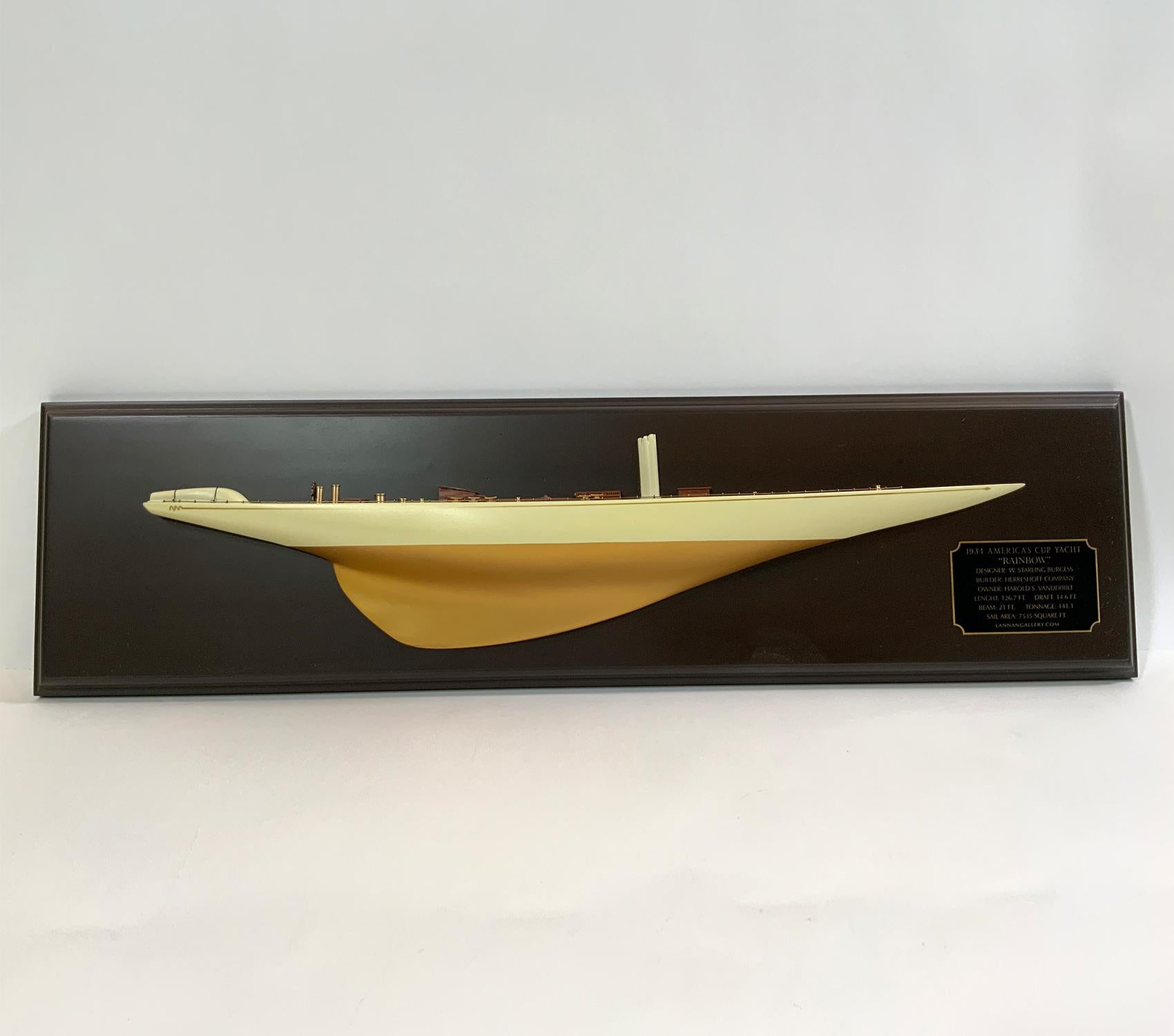 Fine half model of the 1934 America’s Cup Yacht “Rainbow”. This is the here Herreshoff Yacht that won the cup. Hull is painted white over gold. Planked deck with brass details including wheel pedestal, binnacle, compass, etc. There are skylights,