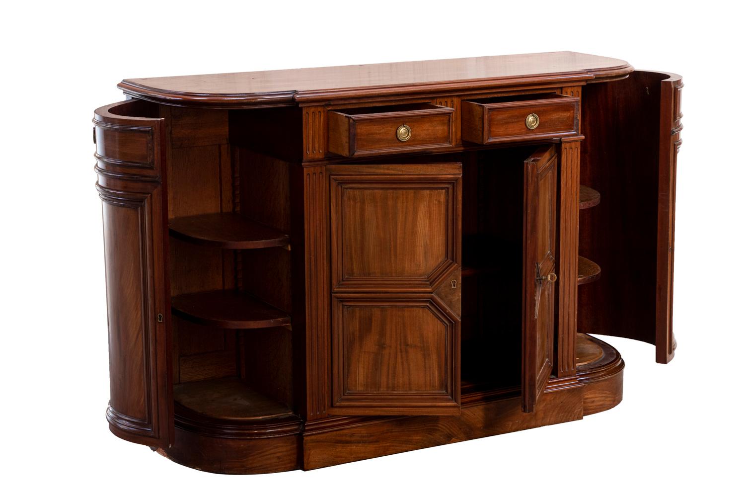 Half-moon buffet in mahogany. Two curved lateral door leaves opening on a compartment with two shelves. Central part with a central breakfront opening by two-door leaves on a compartment with a shelf and by two drawers. Geometrical molded decor on