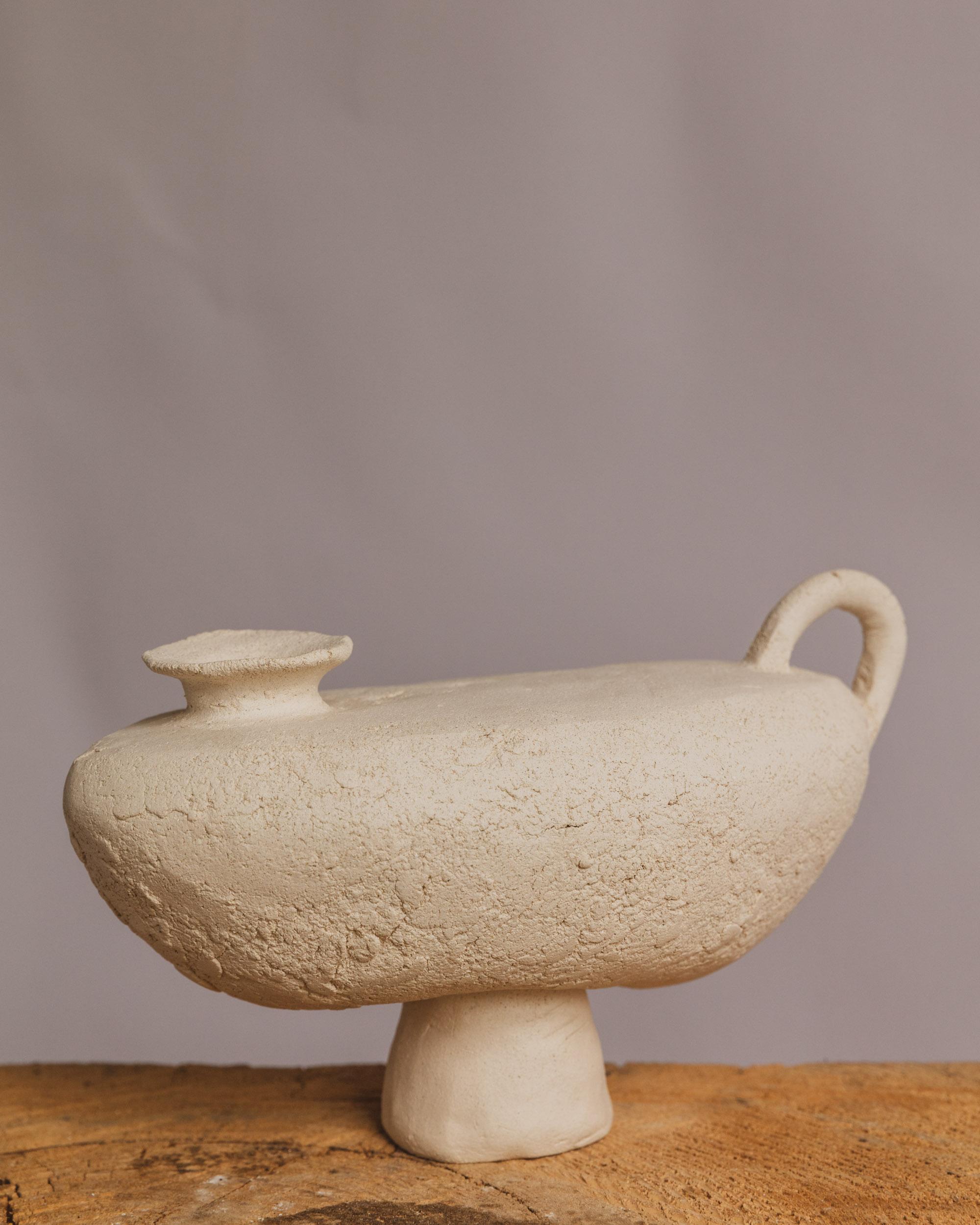 Echoing the silhouette of a celestial arc, Half Moon Jug by Ilona Golovina is a sculptural ceramic vessel that merges ancient symbolism with contemporary restraint. Handbuilt with a textured, matte surface reminiscent of wind-carved stone or dried