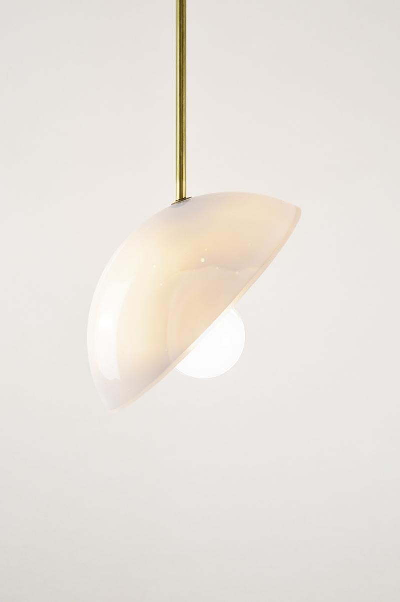 This luminaire, conceptualized by Atelier George in 2020, is part of the Aube collection. This pendant light is inspired by the shape and surface of a half-moon, in opaline white glass, veined with grey and ivory. The luminaire is suspended by a