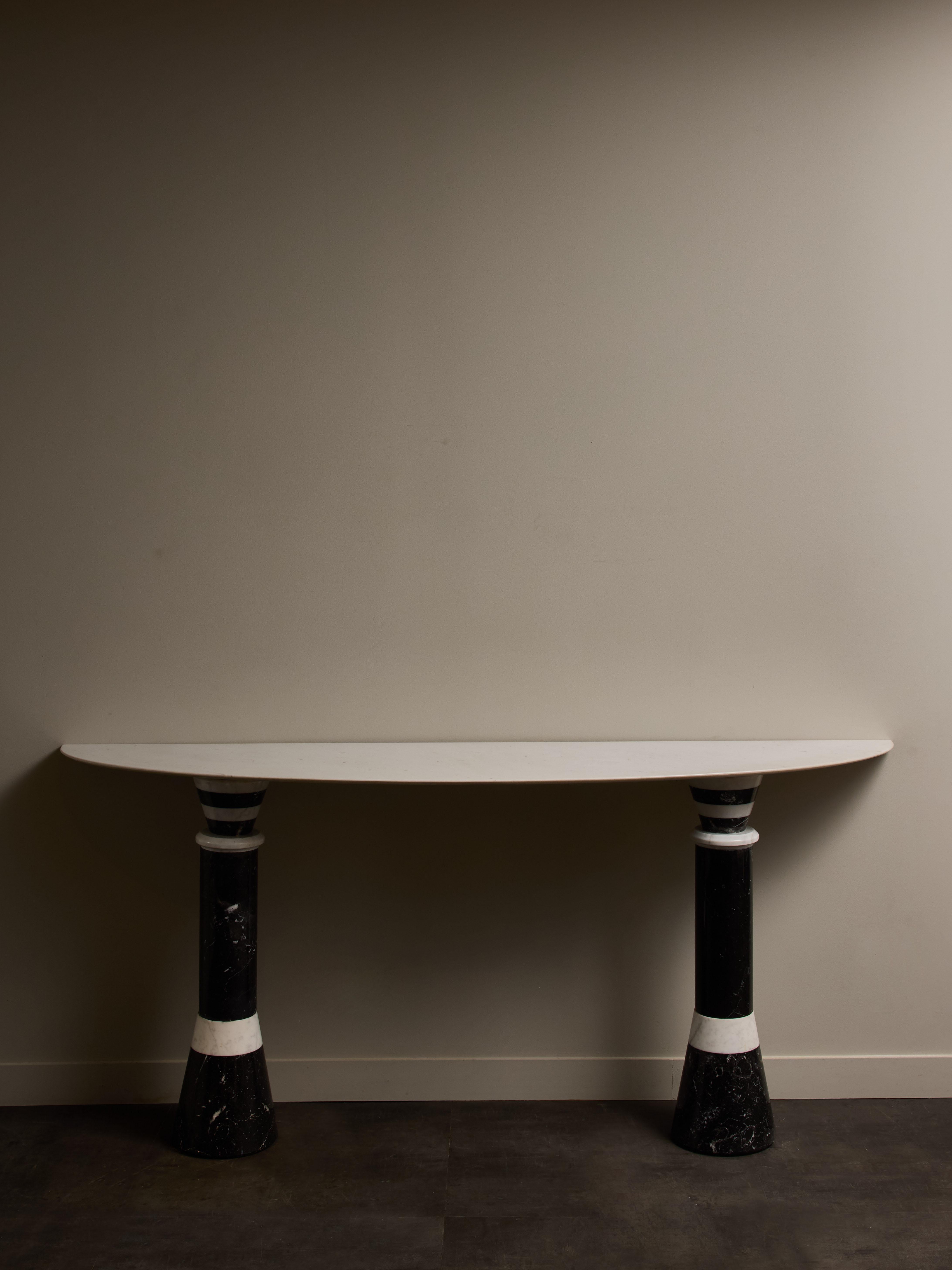 Console italienne vintage en marbre noir et blanc, avec un plateau en demi-lune conçu pour être placé contre un mur.
Les motifs géométriques des pieds évoquent le style caractéristique de Memphis Milano.
