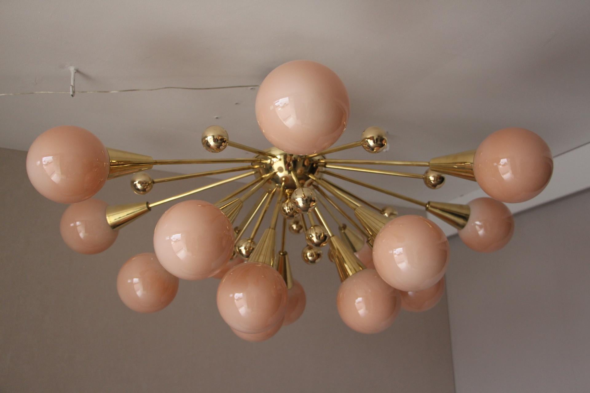 This fabulous chandelier features 15 pinkish-beige handmade Murano glass globes and 15 brass balls extends on brass stems from its centre.
When light is on, its very light pink-beige globes turn to beige color.
All globes are not exactly the same