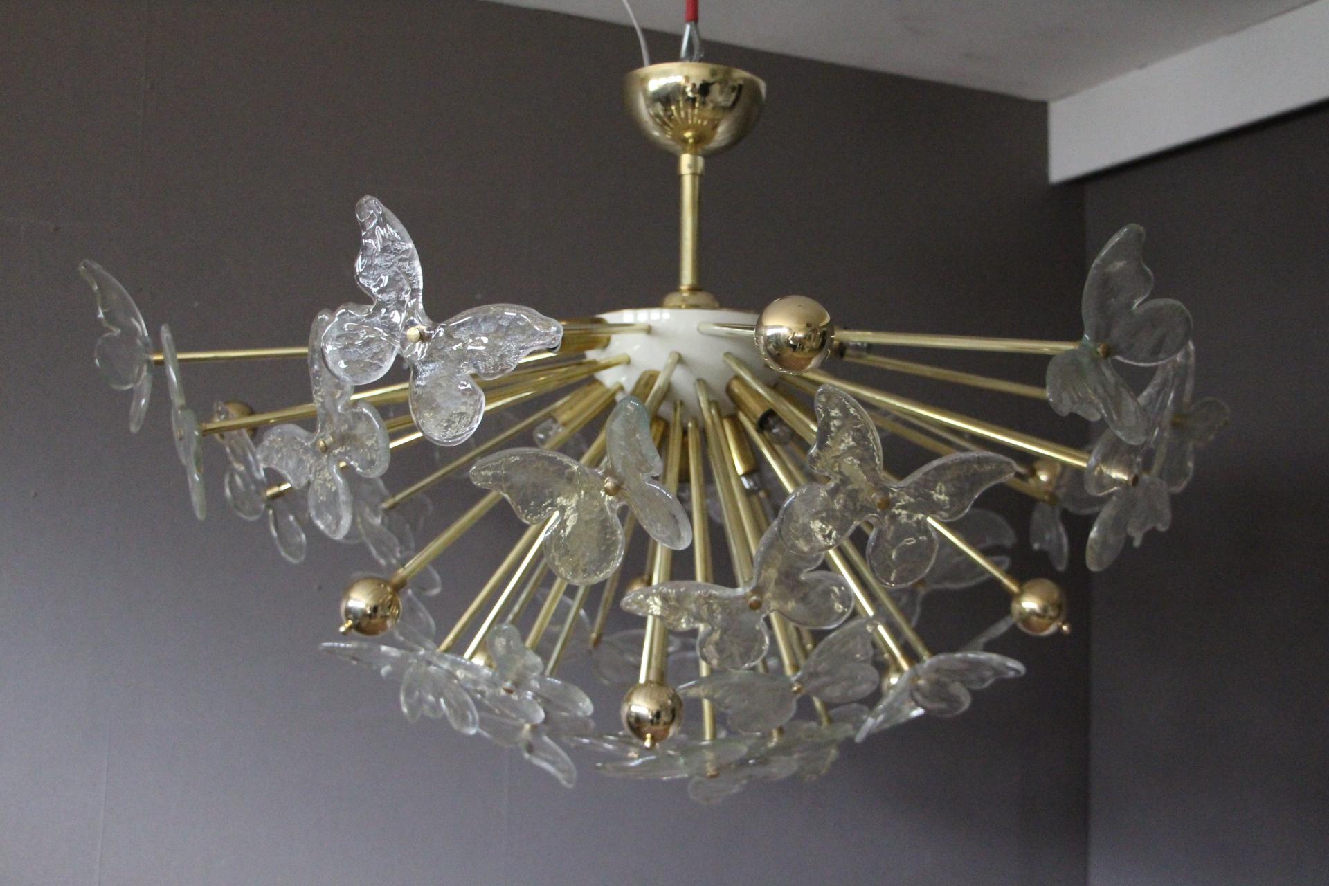 This very unusual half sputnik chandelier features a multitude of brass rods, some ending with brass balls and others ending with flying butterflies in Murano glass.
All the rods have got different length so that butterflies are on different levels