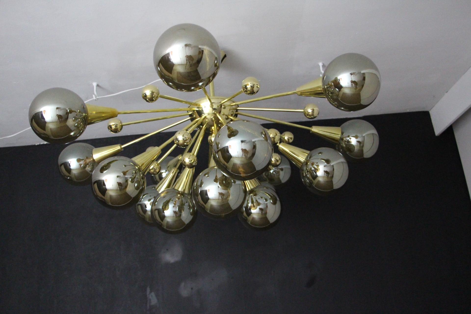This brass chandelier features 15 hand blown half way between gold and silver murano glass globes and 15 brass balls extends on brass stems from its centre. When the light is on, globes change color and become more golden with golden bubbles