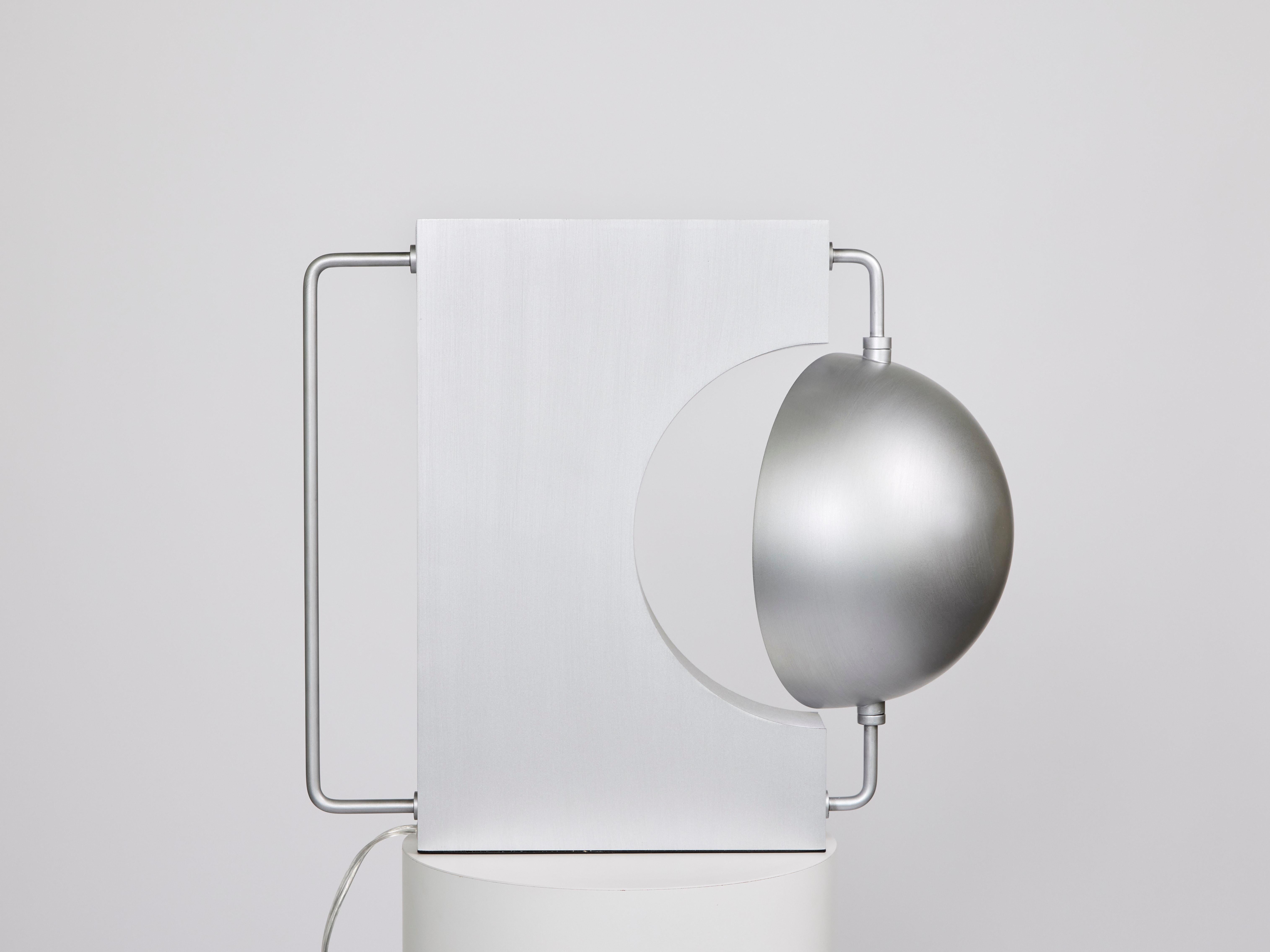 Half Table Lamp (Brushed Aluminum)

Materials: hand-brushed aluminum or powder-coated golden black 
Dimensions: W20 x D11 x H17 inches
Lamping: G9 2700K/3000K dimmable, UL Listed 

A table lamp that plays with contrasting elements of roundness and