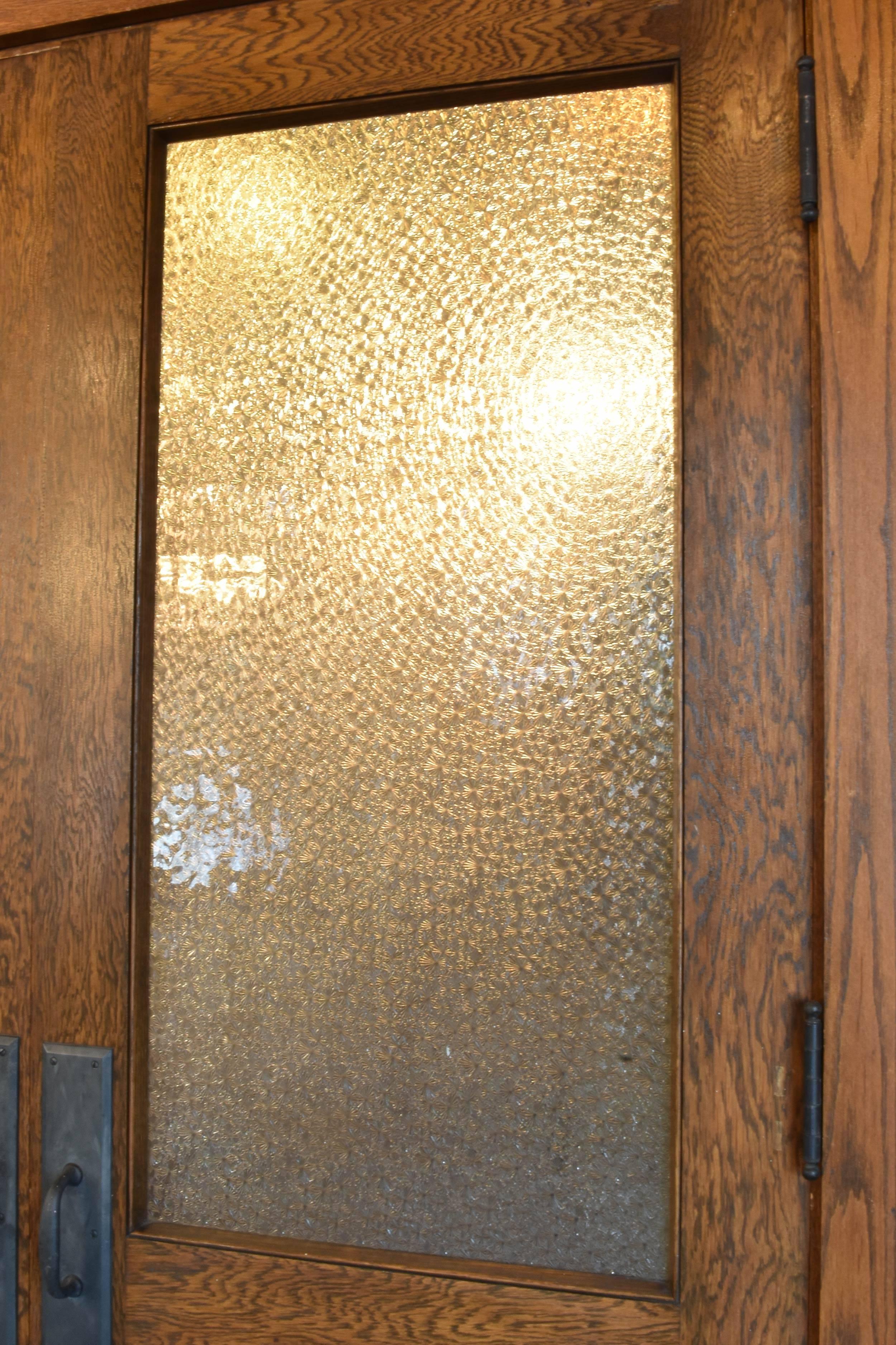 Featuring contrasted wood grain, textured snowflake glass, and iron hardware, these oak double doors are true beauties. The large windows offer natural light to come in while still granting adequate privacy. Originally from a schoolhouse in