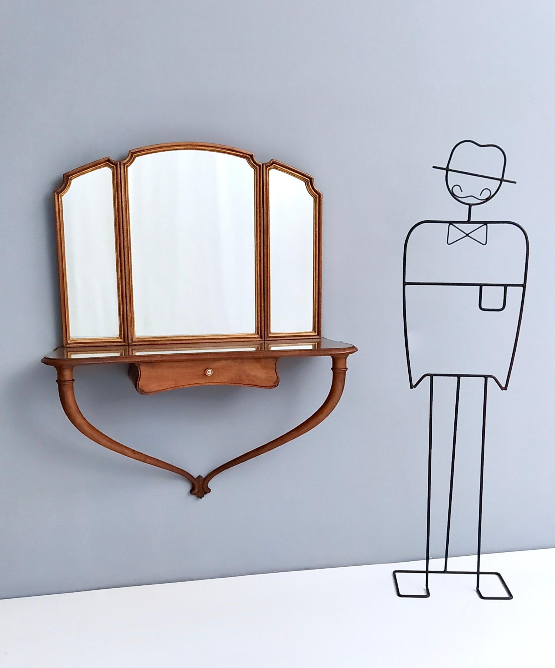 This hallway mirror features a solid walnut frame with gold lacquered details. 
The lateral sections of the mirror are adjustable.
The console table is in solid walnut and features a mahogany drawer with a brass handle and a glass top. 
This is a