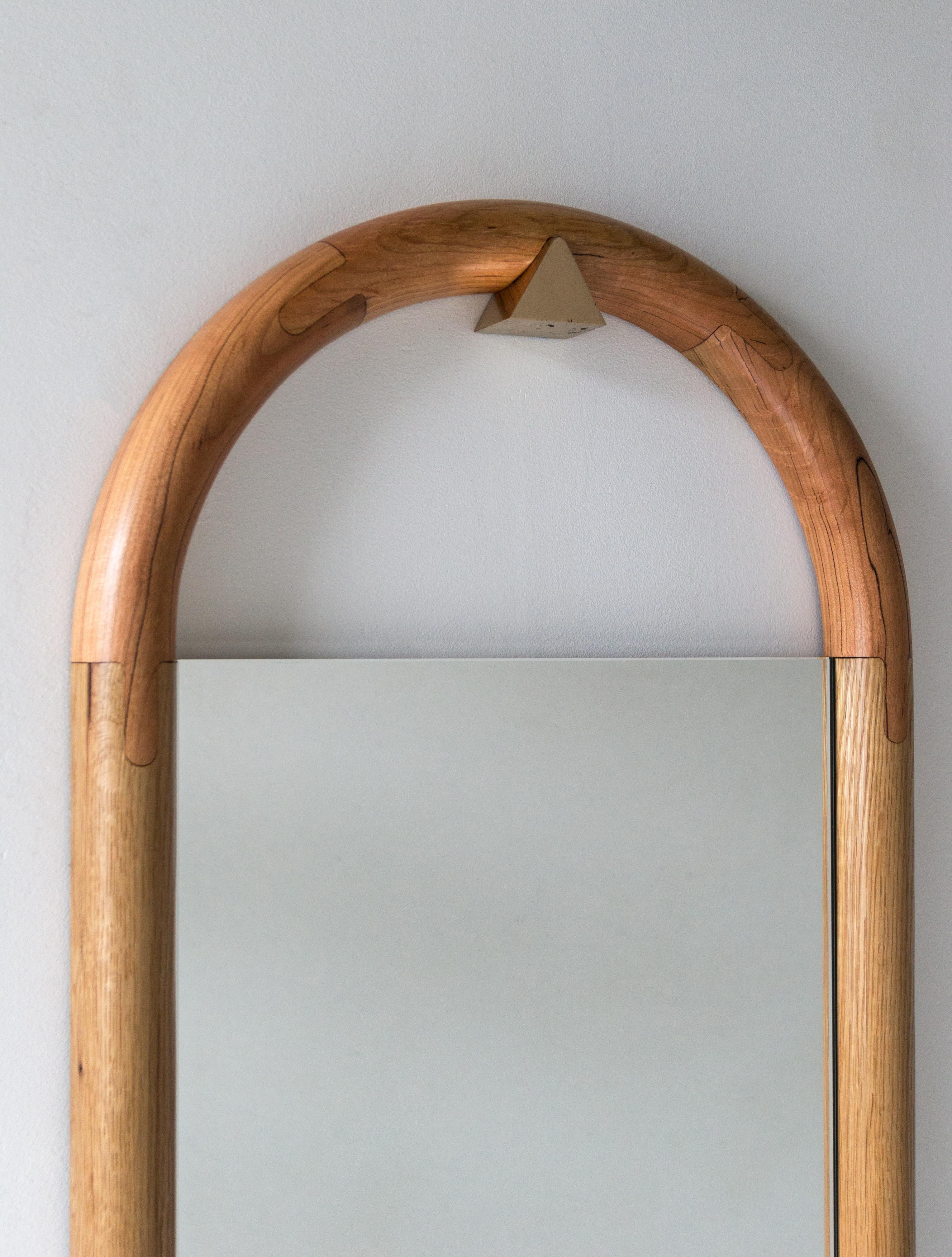 Lo specchio Tall Halo si appende e si autolivella su un piolo triangolare in bronzo. L'assemblaggio di vuoti, tondi e piatti complementari forma una disposizione elegantemente equilibrata di giustapposizione e riflessione. Disponibile anche in altre