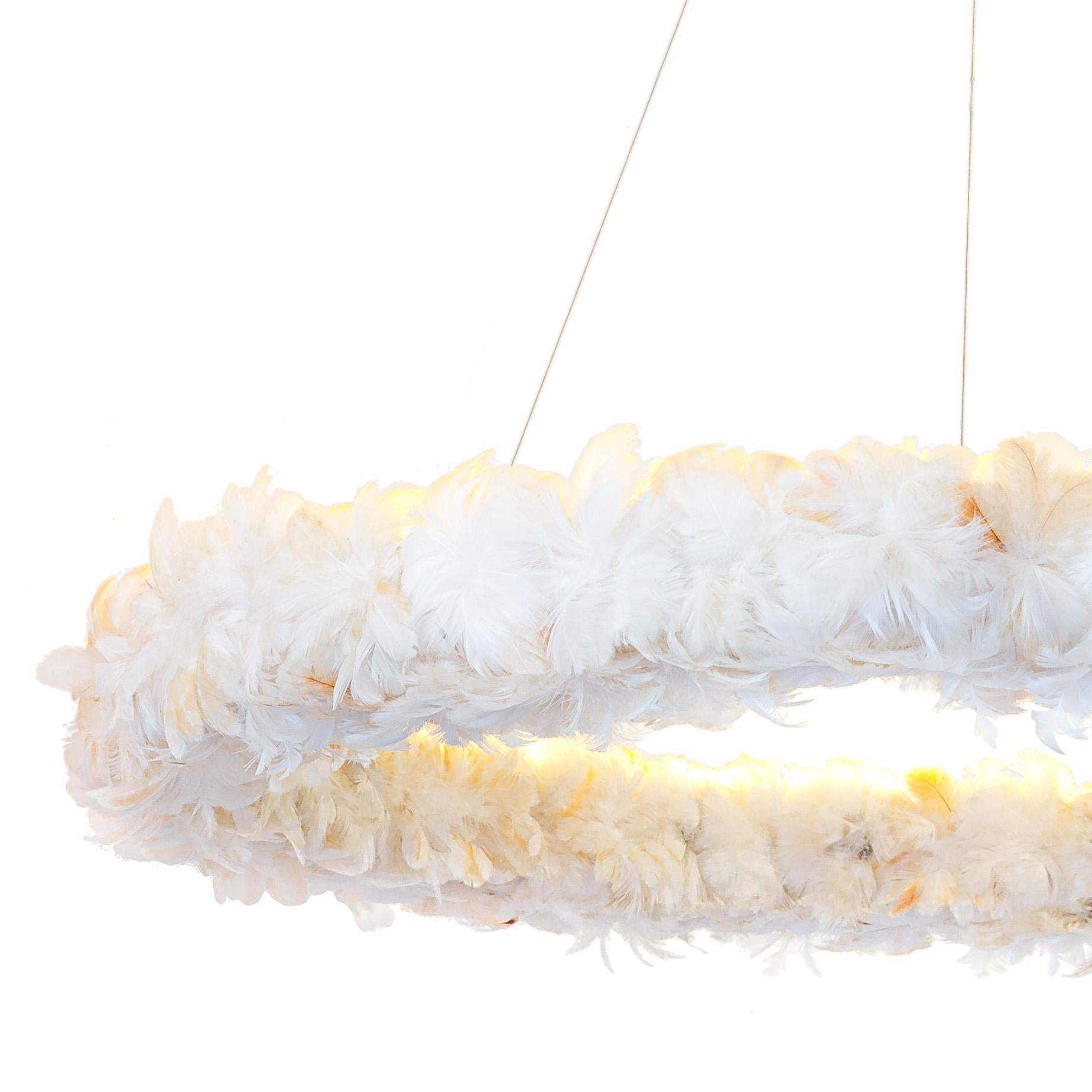 Luminaire à lumière indirecte en bois de peroba recyclé avec des fleurs de plumes entrelacées, offrant un éclairage doux. Suspendu par des câbles d'acier, le Luminaire flotte délicatement dans l'air. 

Inspiré des bandeaux de plumes