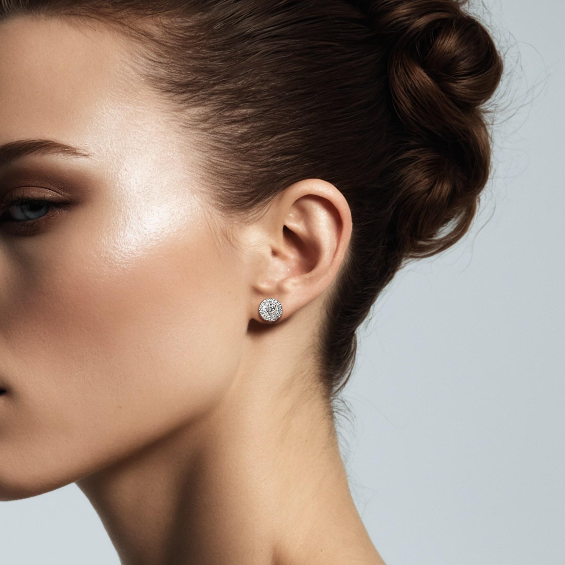 Ces éblouissants clous d'oreilles en forme de halo sont ornés d'une paire de diamants ronds accompagnés de pierres latérales plus petites en diamant rond, le tout serti dans un magnifique halo en or blanc 18 carats. Parfait comme cadeau