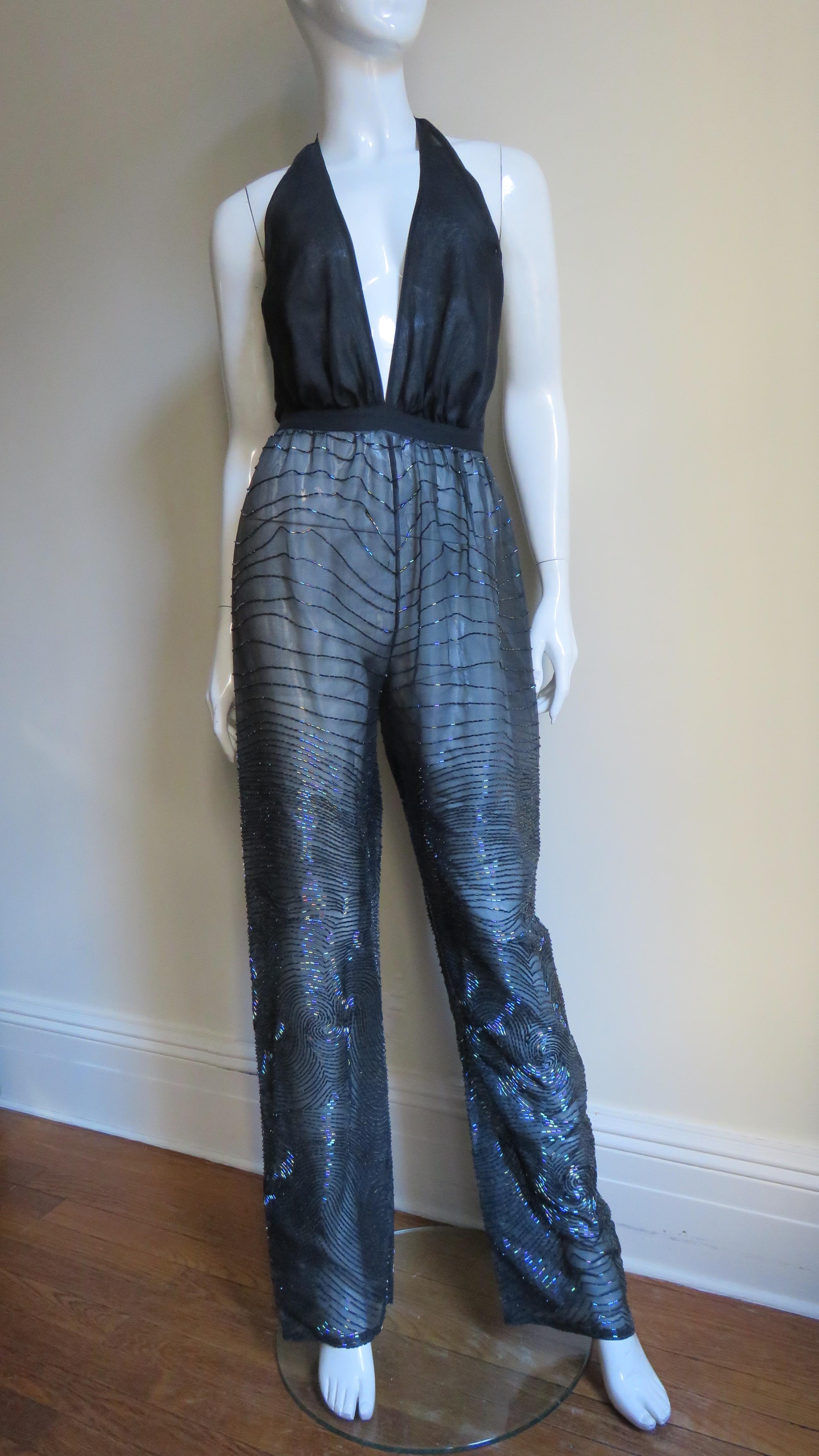 An incredible black silk 2 piece set from Halston covered in an intricately glass tubular bead swirl pattern. The set is comprised of a halter jumpsuit with a deep plunging black silk bodice and straight pant legs. It has a matching beautifully