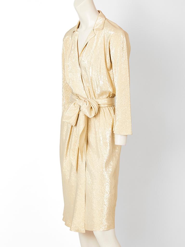 Halston, gold lame, bias cut, wrap dress, having a deep V, with small collar, long sleeves and a self belt/ sash that can be tied at the waist to be made into a generous bow. C. 1970's.