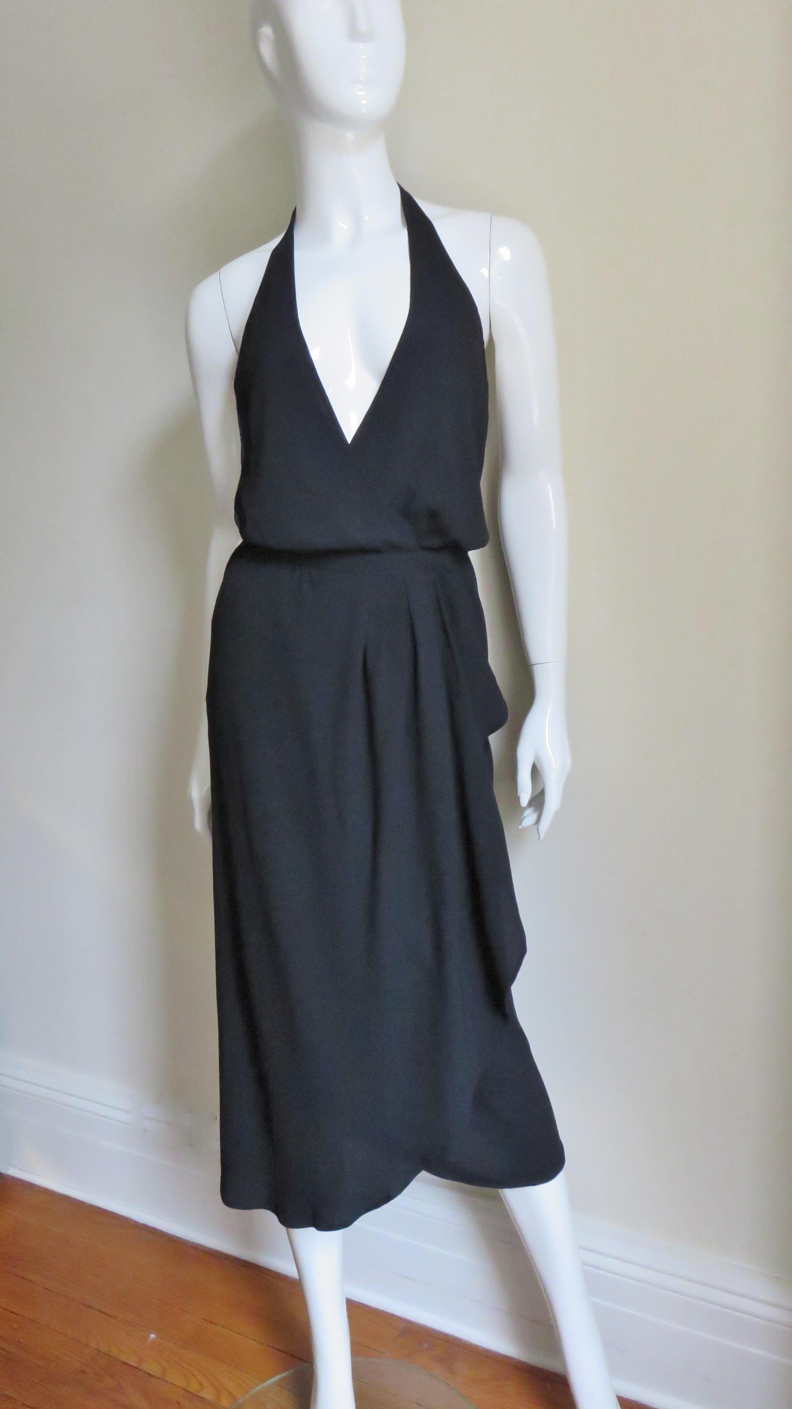 A black silk halter wrap vintage dress from Halston. It has a plunging halter neckline and a low cut back.  The dress crosses in the front and wraps to the side secured with large hooks on the 1' waistband. The skirt lightly gathers at the waistband