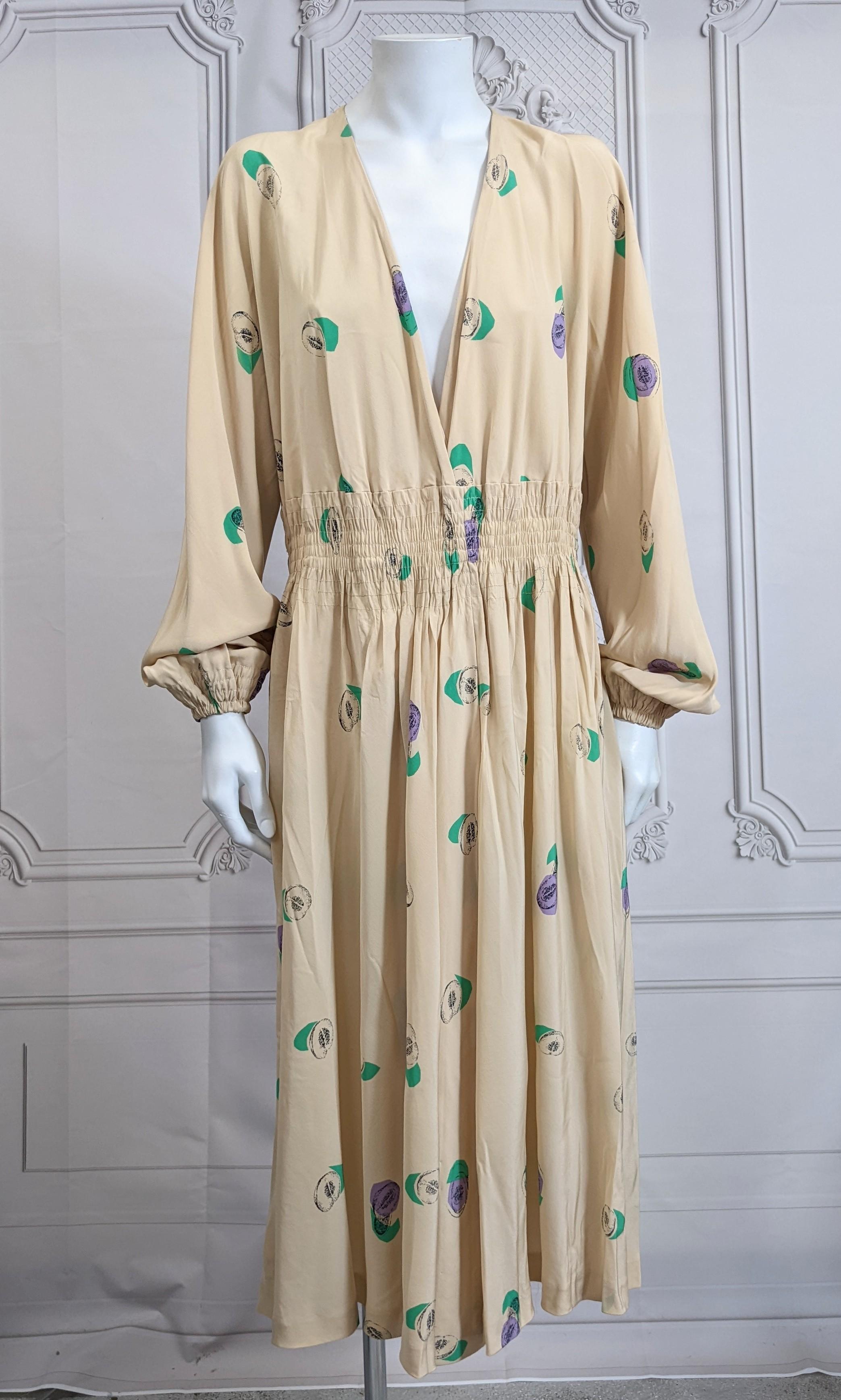 Halston's Deceptively Easy Pullover Silk Crepe Faux Wrap Dress printed with colorful pomegranates on a beige ground. Designed as a faux wrap dress which is closed at the waist in a simple pullover style. 
Deep V neckline meets with overlapped slit