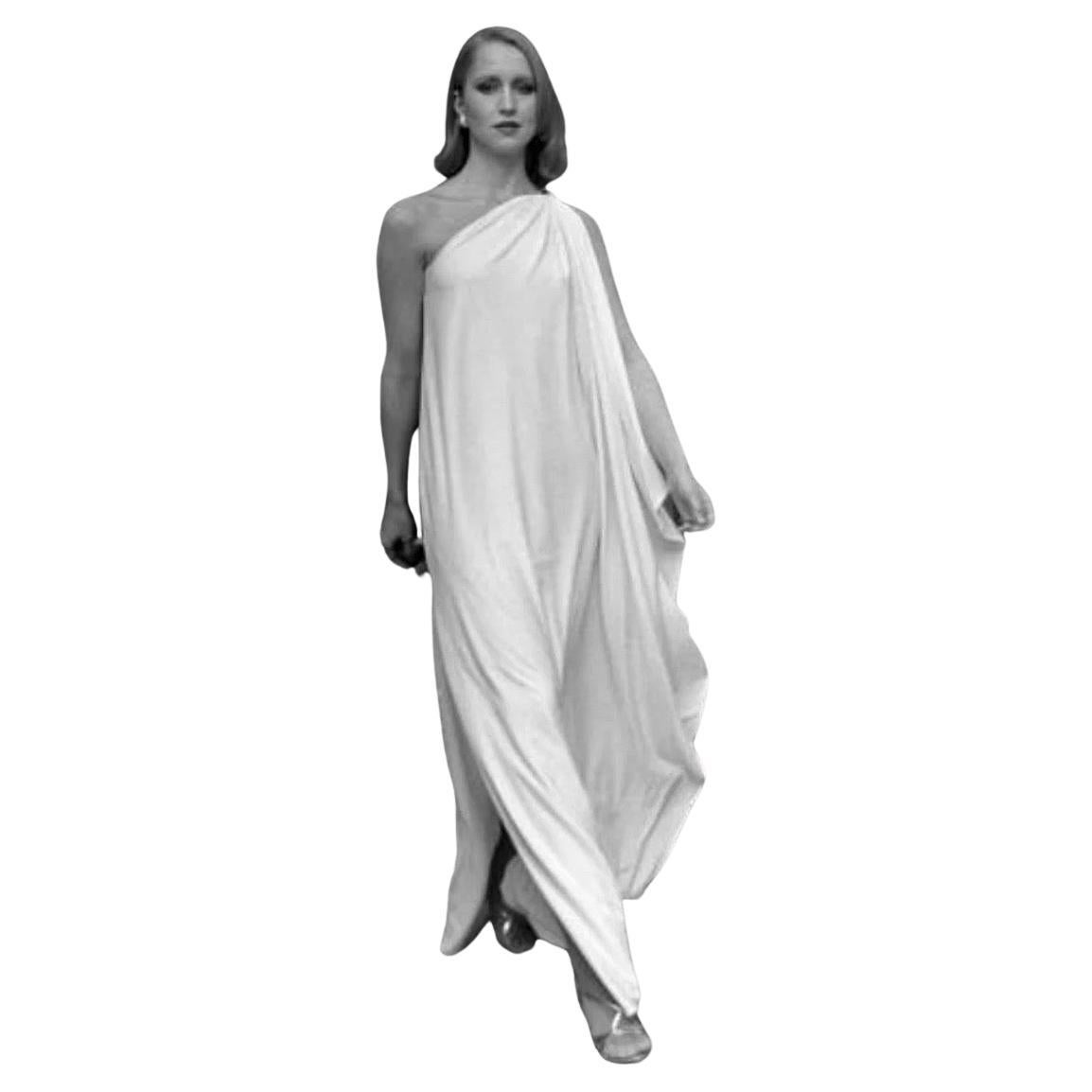 An iconic piece from Halston’s late 1970s body of work, this white one-shoulder gown embodies his signature draping and minimalist glamour. Cut in fluid jersey, the gown features a Grecian-inspired silhouette with asymmetrical shoulder, clean lines,