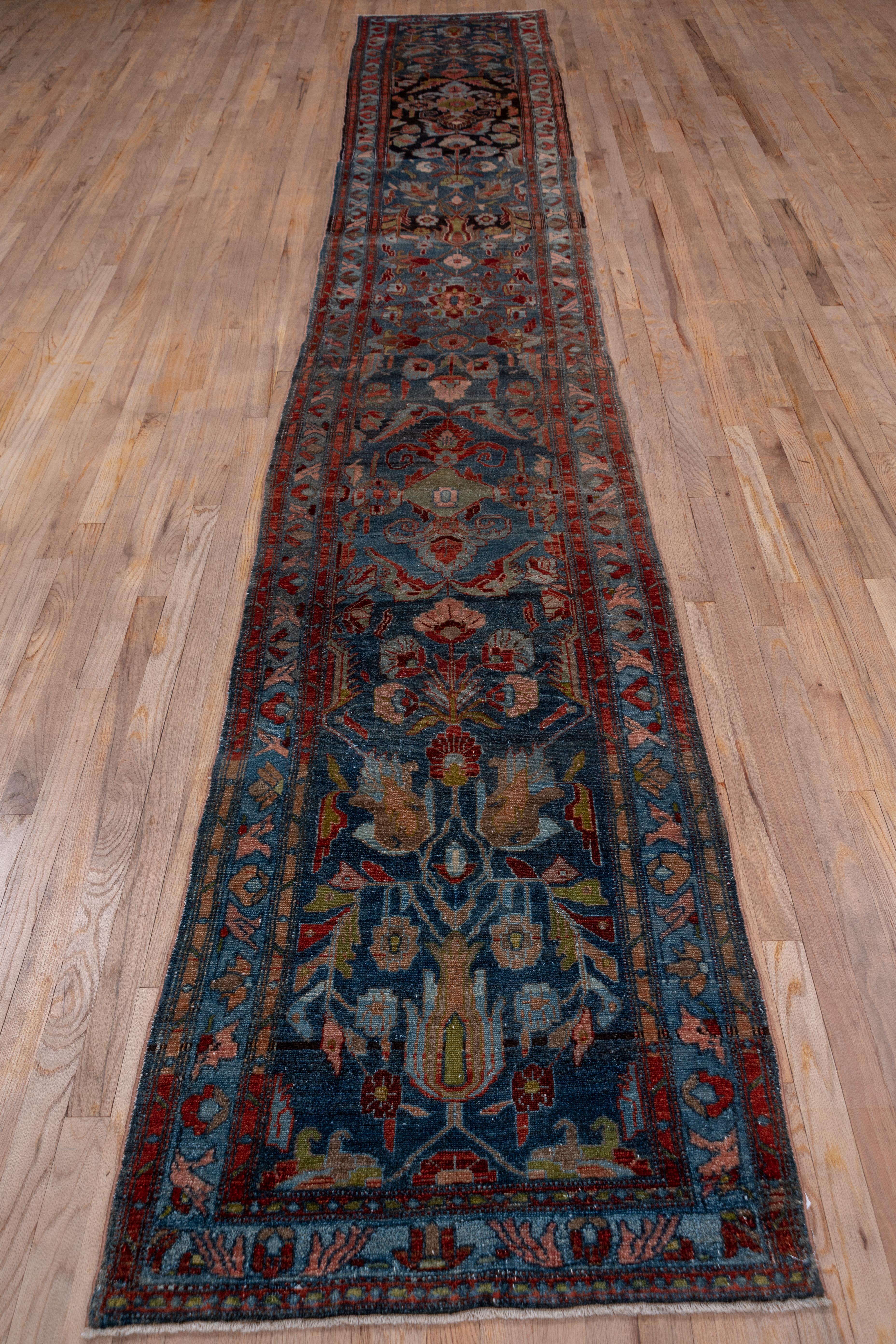This rather flat west Persian runner displays an abrashed green to deep blue-green field with a giant flower and leaf pattern in dark brown, light blue, rust and golden-brown. The medium blue border displays a very simple palmette and diagonal leaf