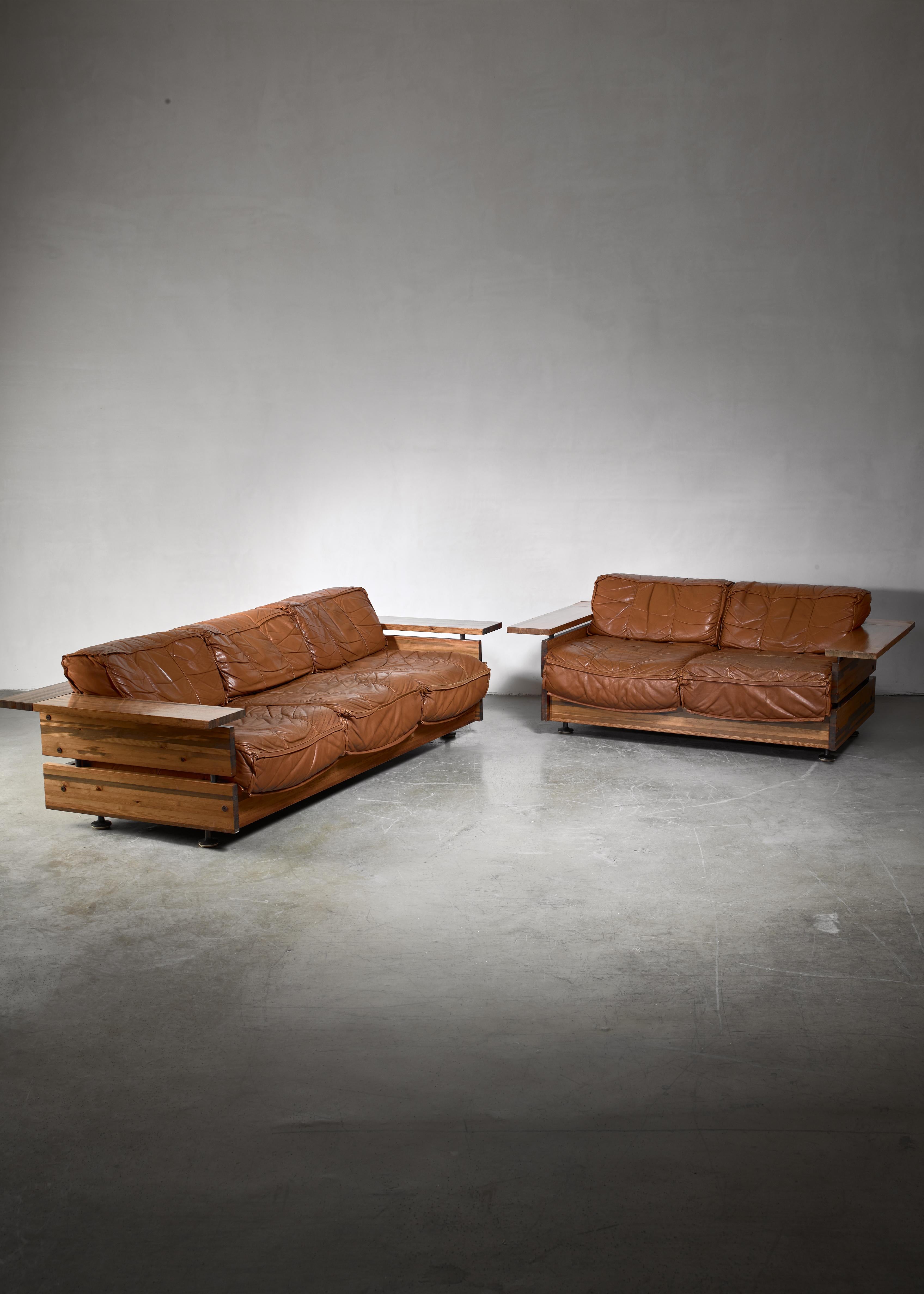 A Finnish sofa set by Hämeen Kalustaja. The three-seat and two-seat sofa are made of stained pine with brown leather cushions.

The measurements stated are of the larger sofa. The two-seat is 168 cm wide. Marked by Hämeen Kalustaja.
 