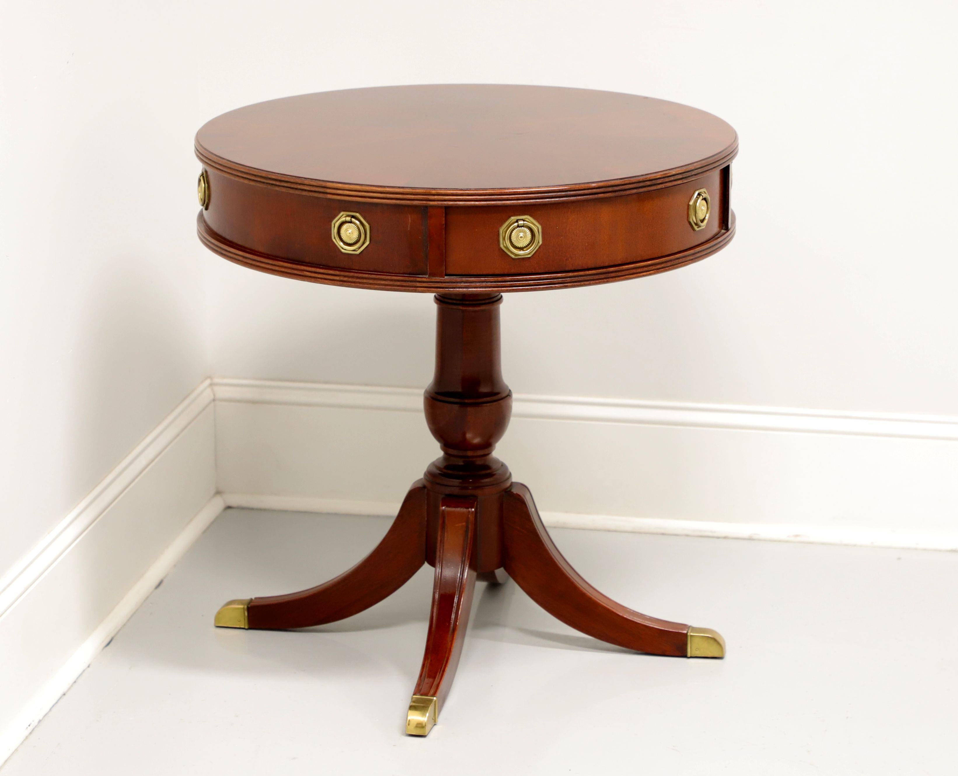 A Traditional style round drum table by Hammary Furniture. Mahogany with banded & inlaid top, brass hardware, turned pedestal base and four legs with brass toe caps. Features one working dovetail drawer and three faux drawer fronts. Likely made in