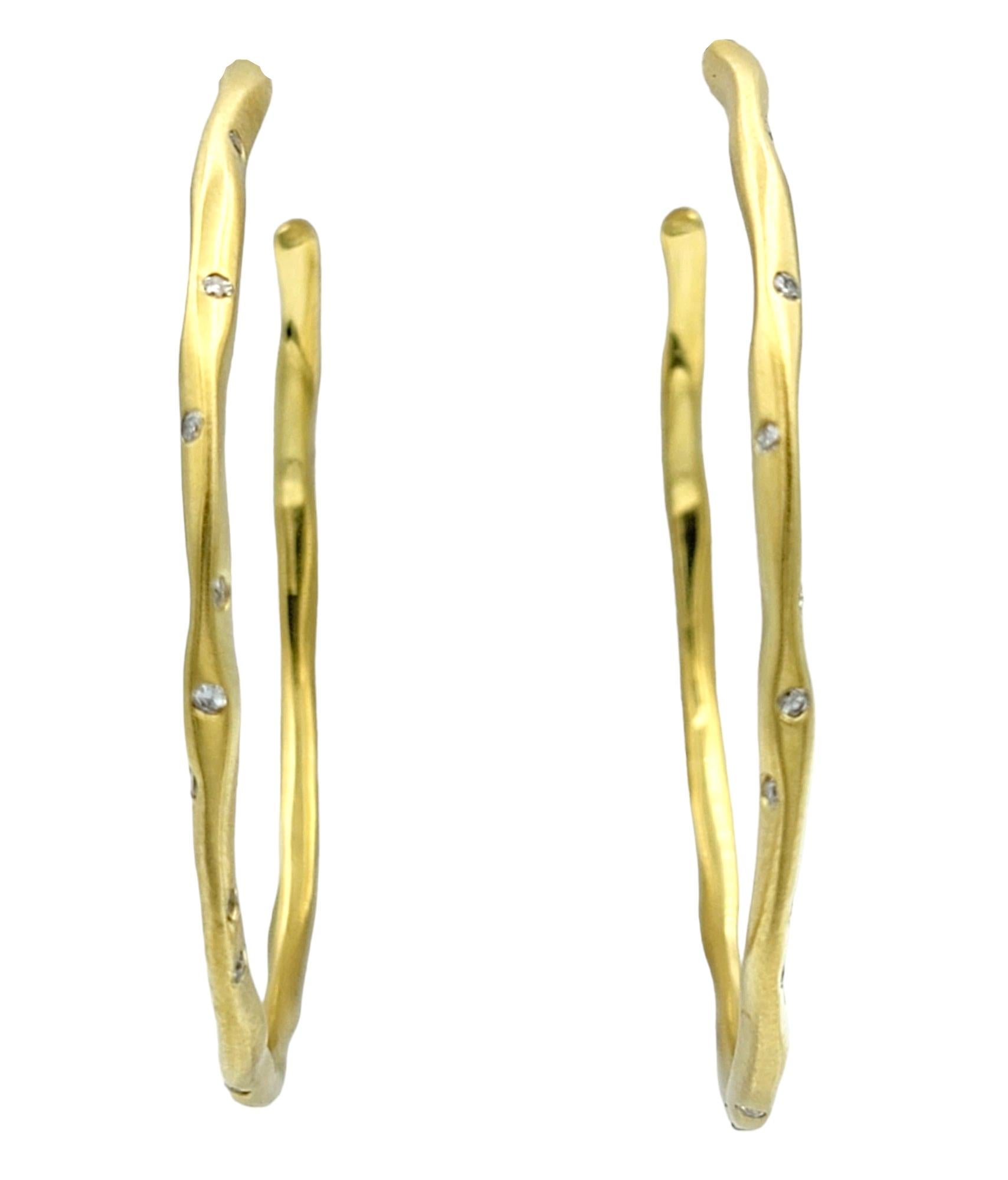 These dazzling diamond hoop earrings, set in luxurious 18 karat yellow gold, exude a modern and refined elegance. The sizeable hoops are done in a brushed finish with a hammered design, giving a contemporary and unique element to the pair. Scattered