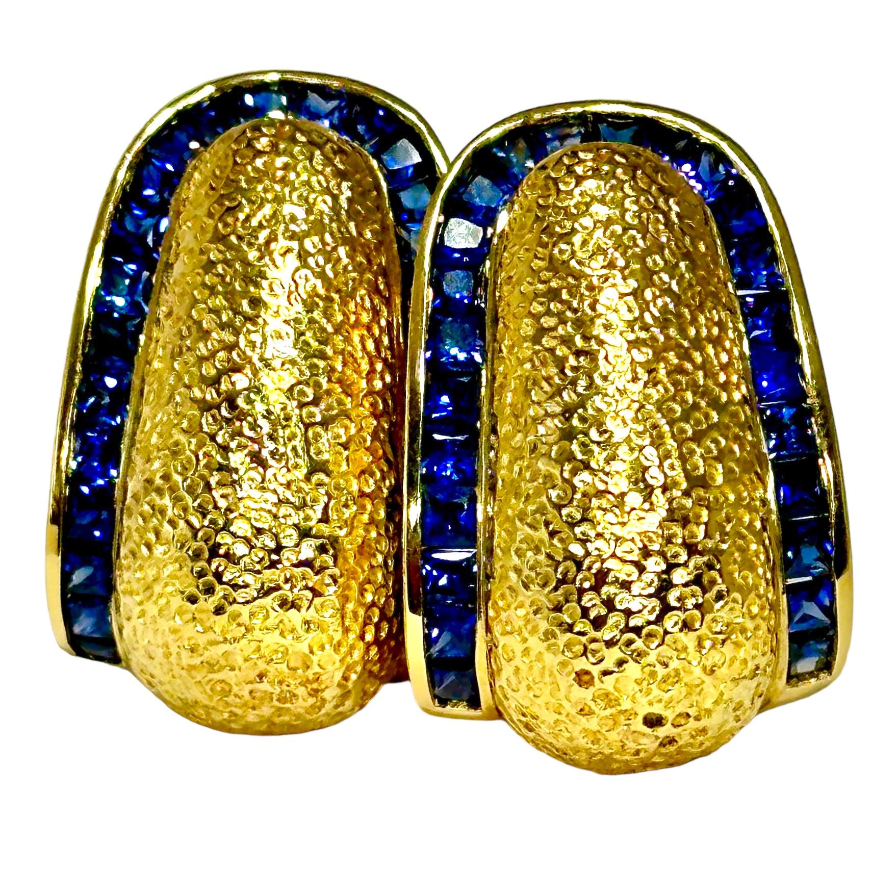 With a designer style to them, these handsome earrings are fashioned in richly colored 18K yellow gold with vivid blue sapphire borders. At the center of each earring is a bombe' section, beautifully finished with a micro-hammered texture. Framing