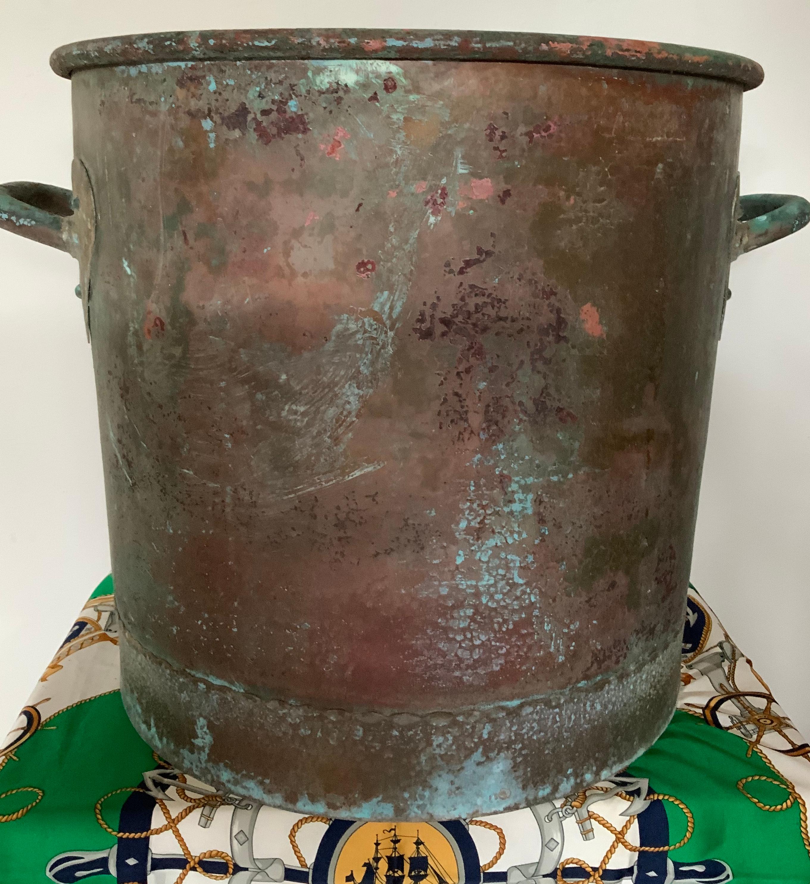 Huge, round, and heavy copper cauldron with two heart shaped brackets holding handle rings. Highlighted by his natural patina of years of use. The lower bottom is embellished with scalloped border decor.
