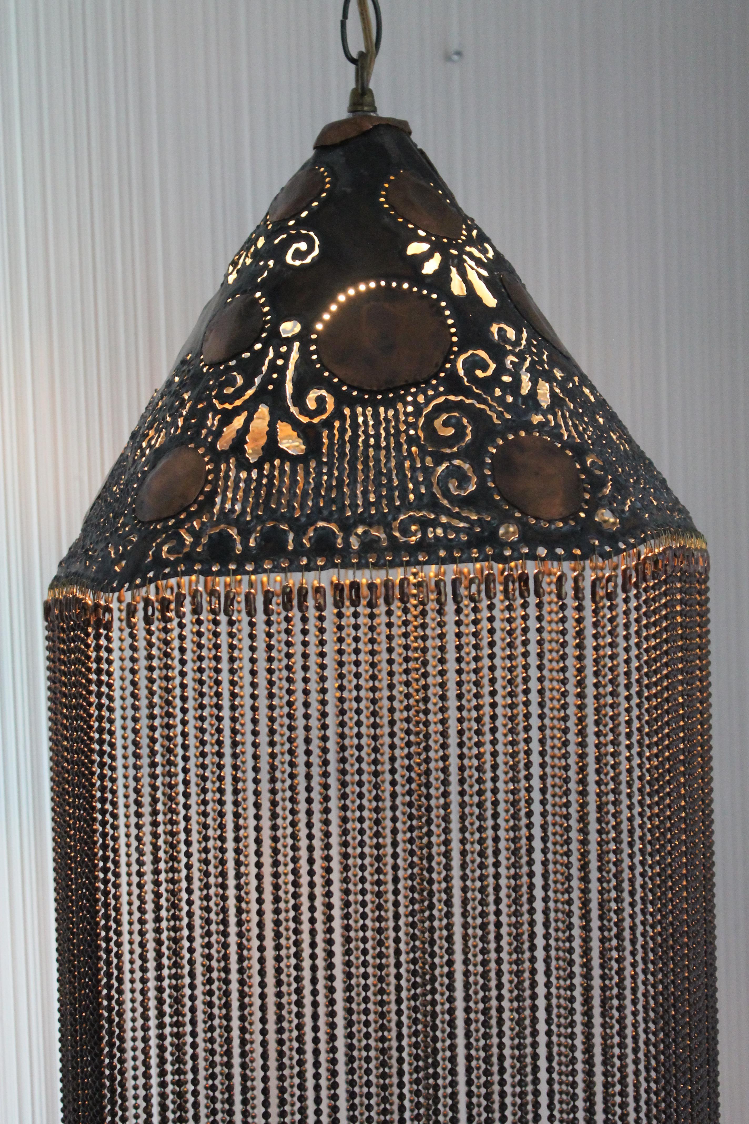 A vintage handcrafted hanging fixture, dated 1977. The cone shaped shade is heavily pierced with psychedelic flower shaped cutouts. Fixture is 30