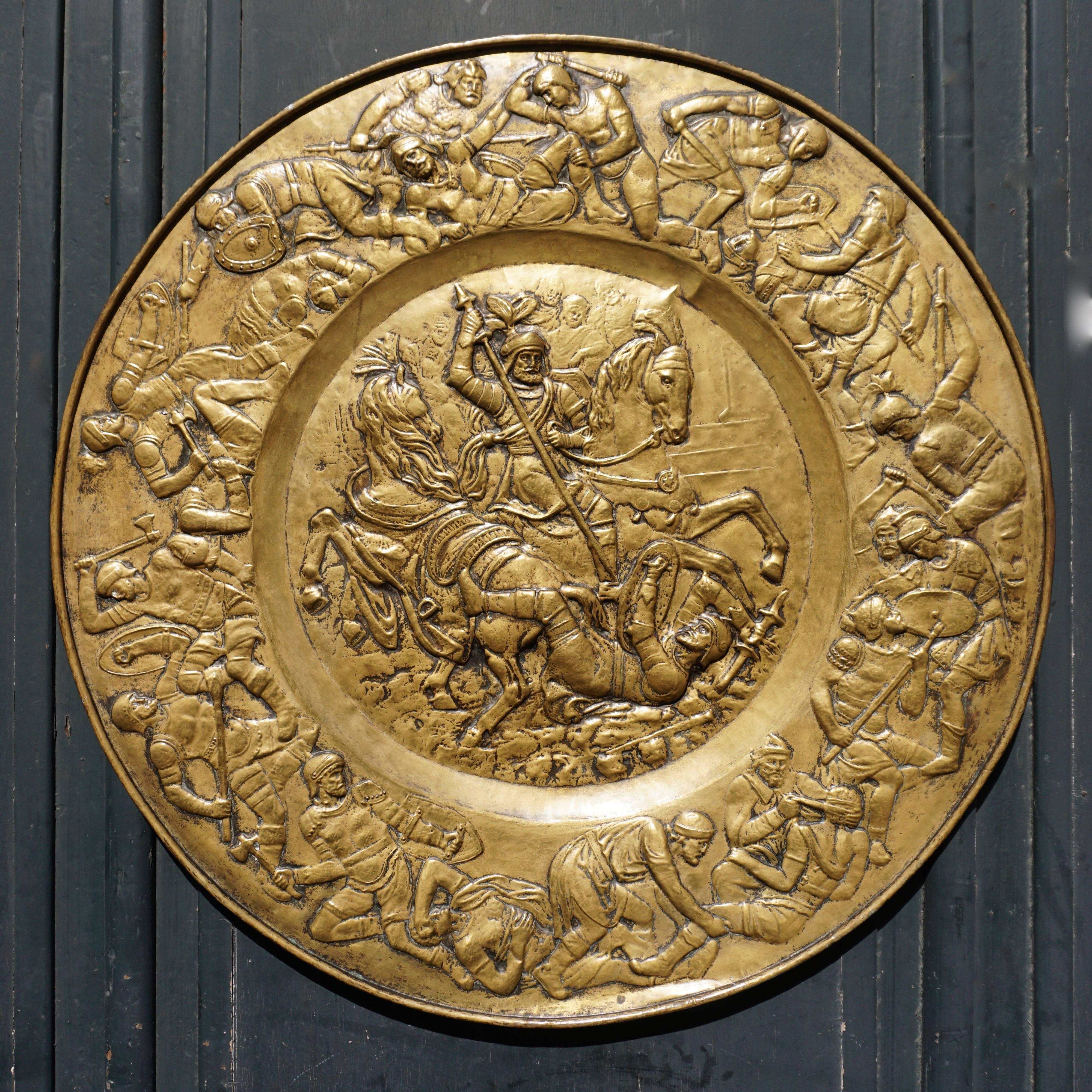A 19th century hammered brass dish of unusual size in the historical style representing a battle scene between Romans and Barbarians, in the middle fighting generals on horseback, the frieze surrounding them showing infantry engaged in battle and