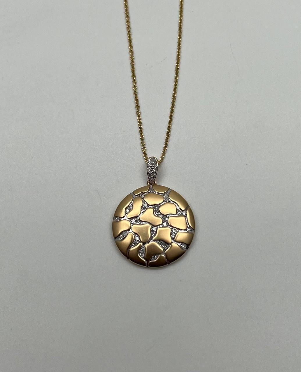 Un superbe collier à pendentifs. Cette pièce exquise présente un pendentif rond au design abstrait unique. Le pendentif présente une surface dorée avec des motifs complexes et irréguliers ressemblant à de la terre craquelée, accentués par des
