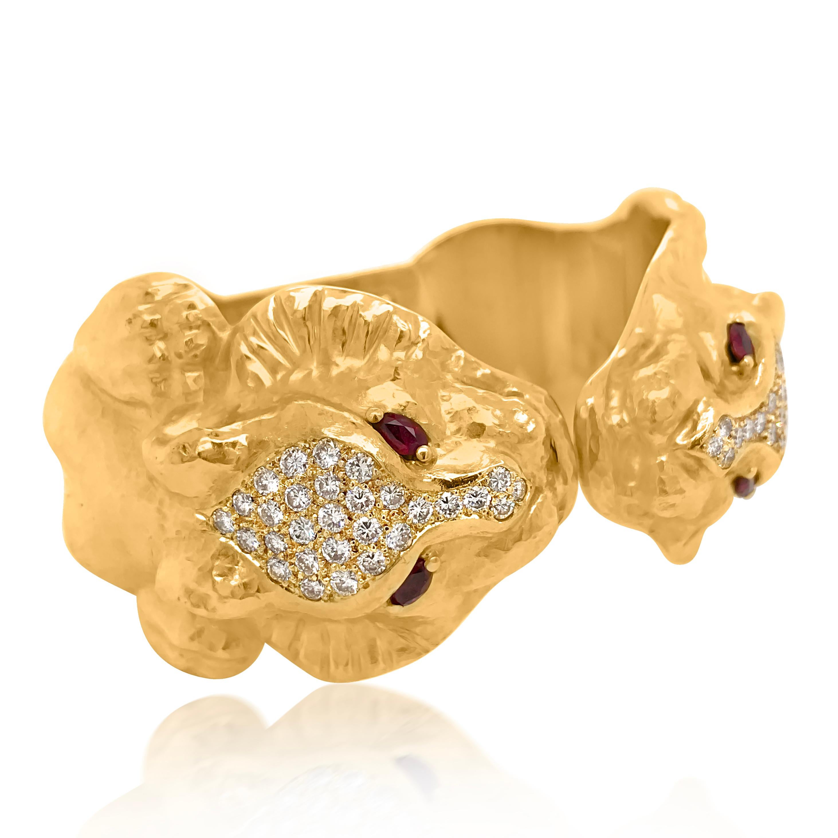 This vintage cuff bangle bracelet is hinged hammered gold cuff terminating in a pair of lion heads, centering fancy-shaped panels pave-set with 58 round diamonds approximately 2.15 cts., accented by 4 marquise-shaped ruby eyes. The bracelet weighs