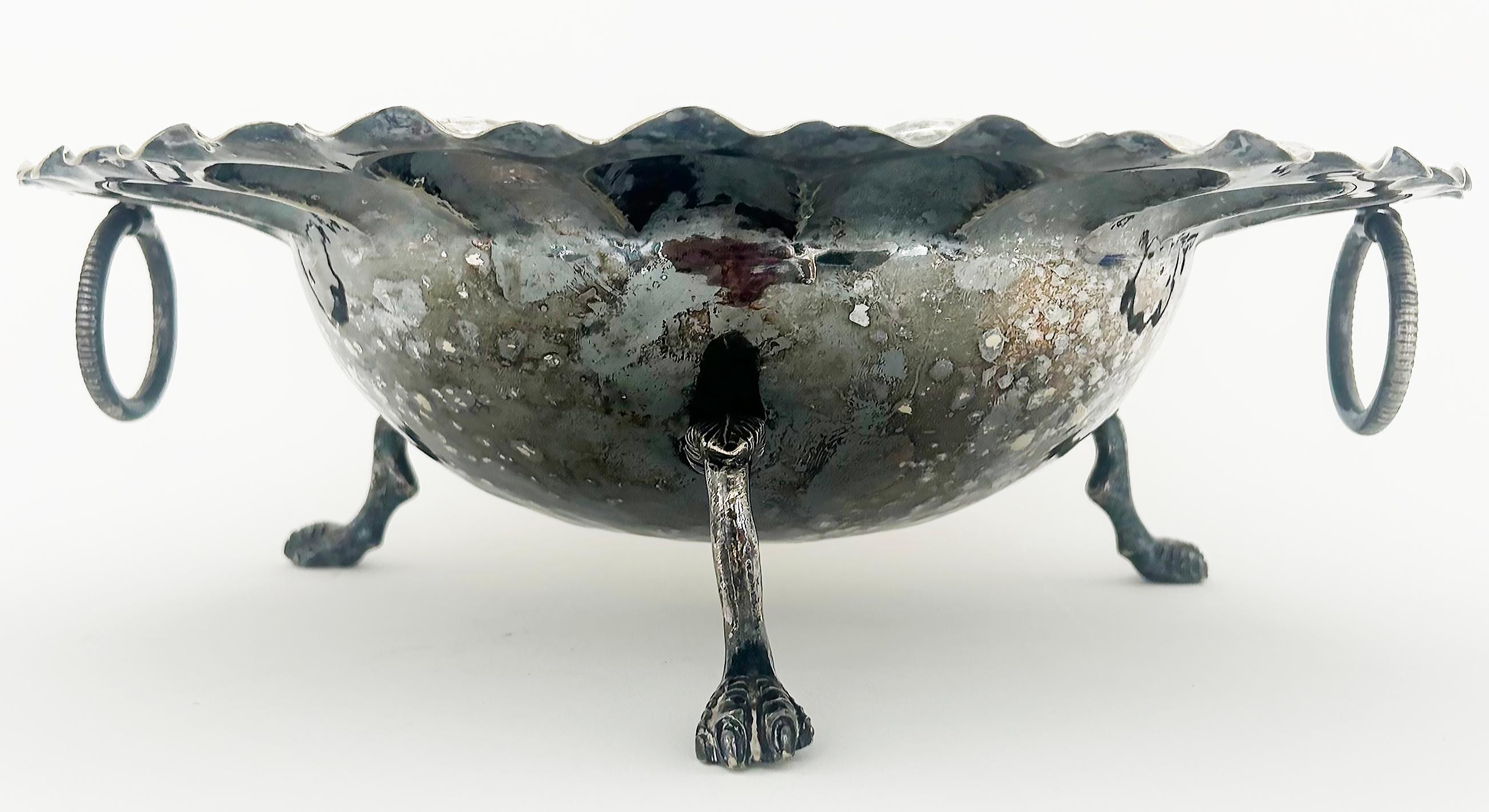 Ciotola con piede in argento martellato con bordo smerlato e manici ad anello

In vendita c'è una ciotola decorativa con piedini in silver-plate con un elaborato bordo smerlato. La ciotola è sostenuta da 3 delicate gambe con piedi a tre dita. I lati