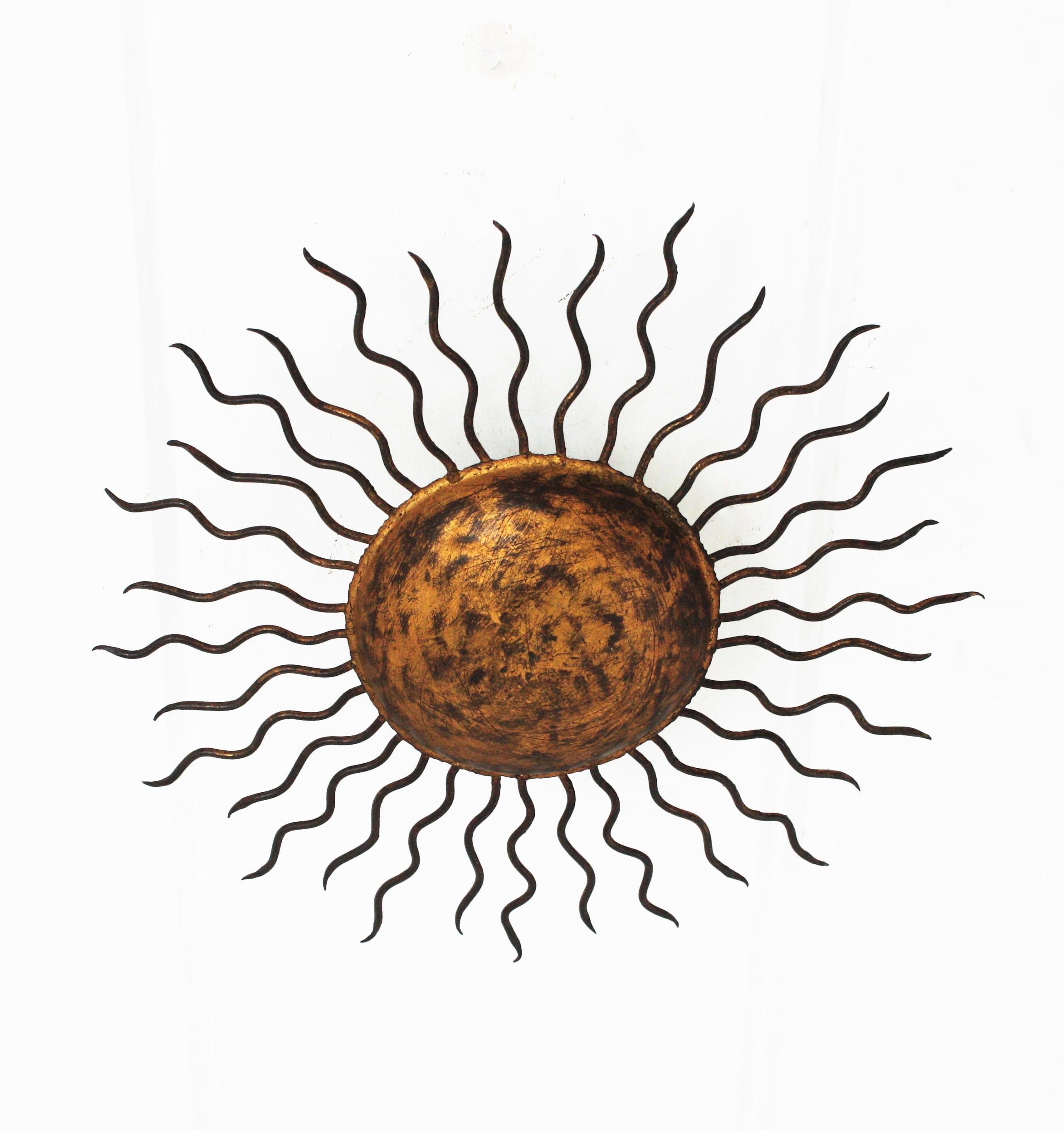 Handgehämmerte Sonnenschliff-Leuchte aus vergoldetem Eisen mit brutalistischen Akzenten. Reichhaltig verziert mit handgehämmerten Marken, Spanien, 1950er Jahre.
Es hat gelockte Eisenstrahlen in zwei Größen, die eine zentrale große Kugel umgeben. Sie