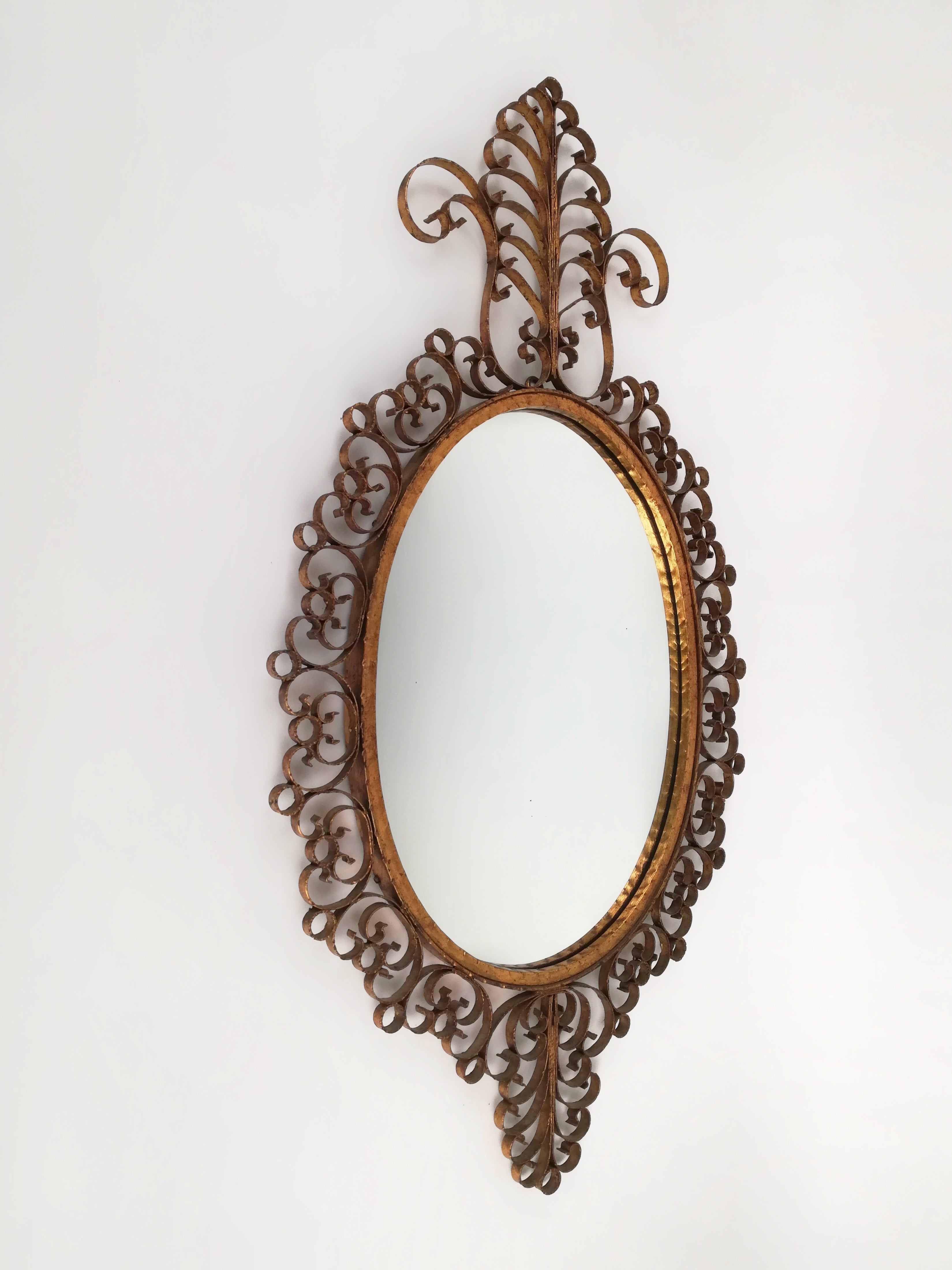 Grand miroir (Hauteur 117cm) d'inspiration baroque, fabriqué à la main en Italie dans les années 1950 dans le style des produits Pierluigi Colli.
La structure en fer forgé est décorée à la feuille d'or ; les courbes et les volutes en métal martelé