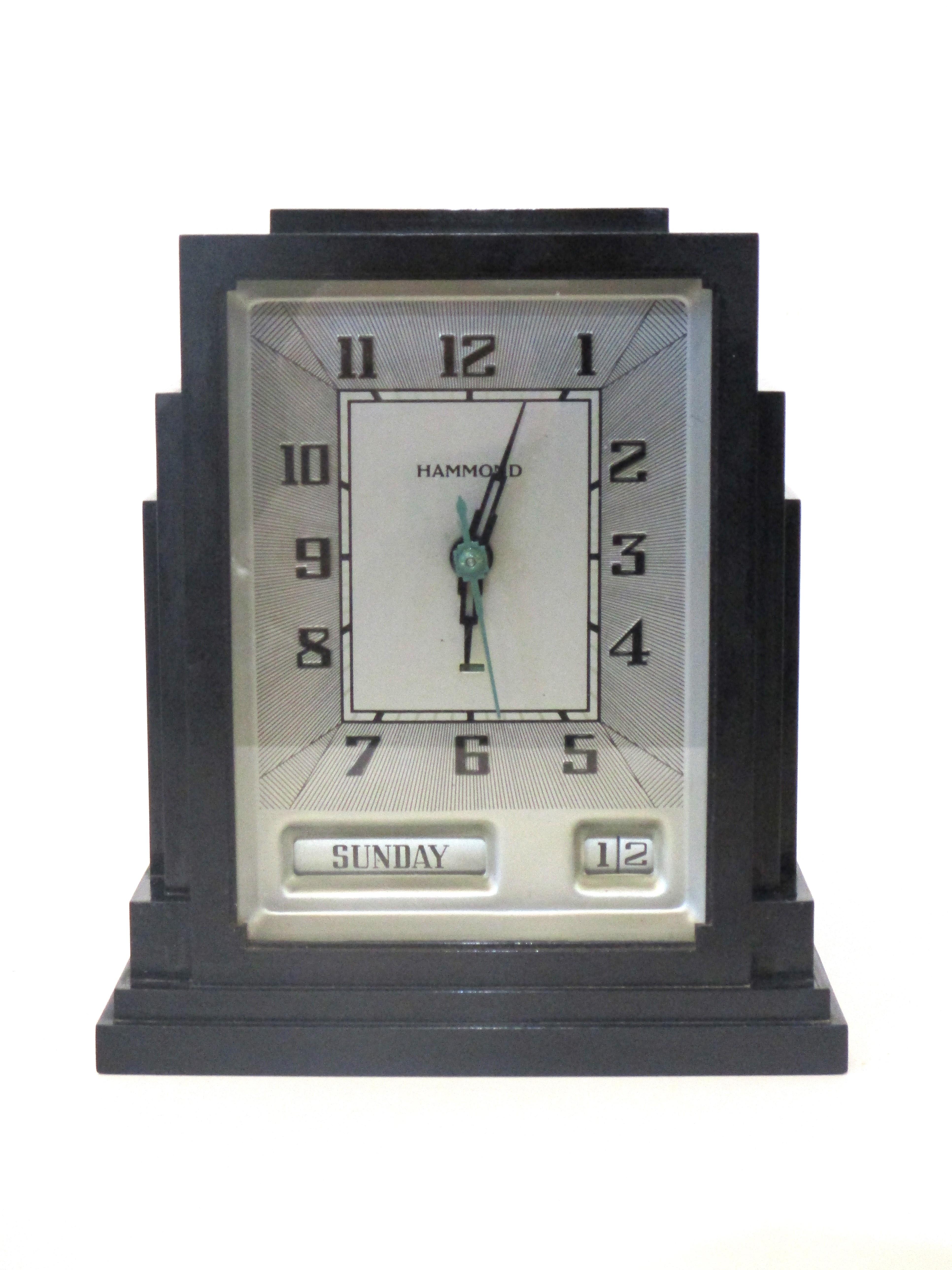 A rare day and date Art Deco skyscraper styled clock with dark bakelite case and metal face with black and green skyscraper hands. The lower area has the day and date which make this clock unique, manufactured by the Hammond Clock company known for