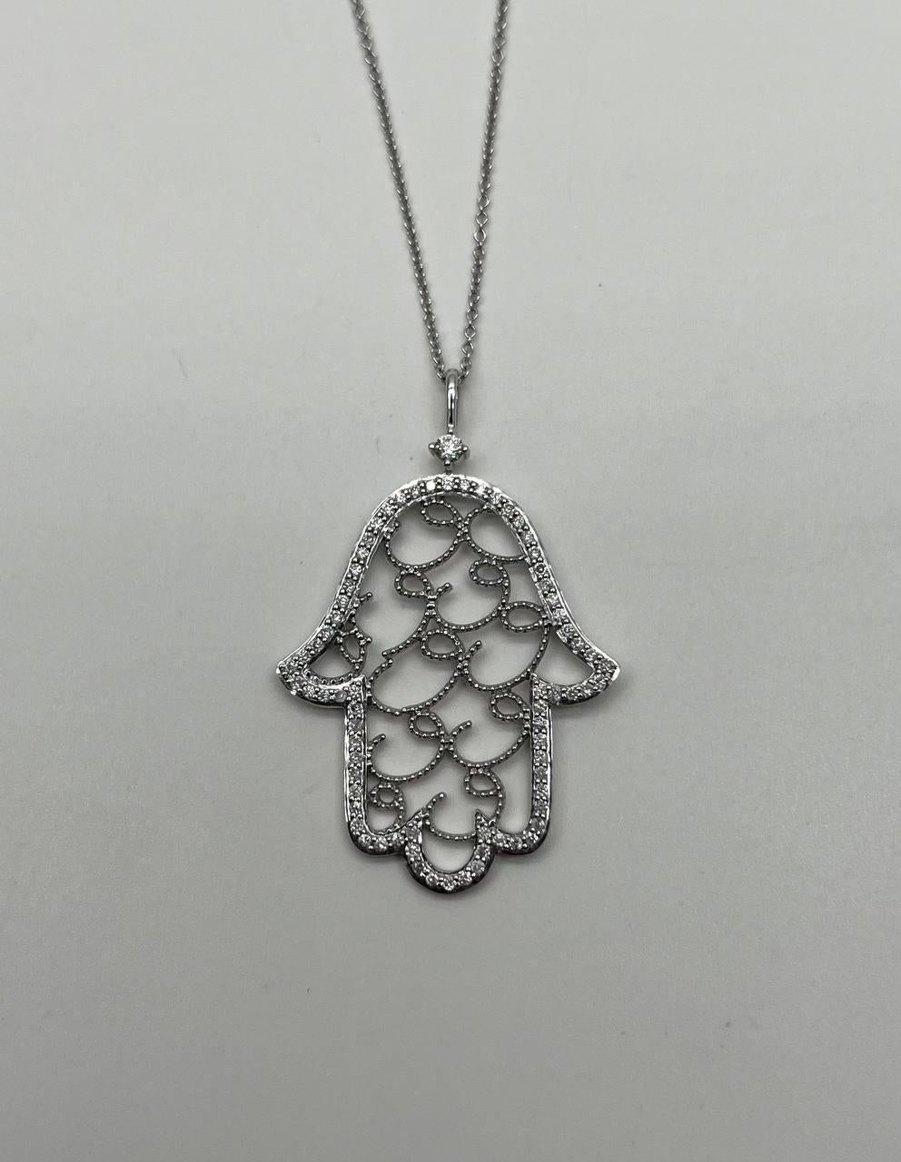 A stunning pendant necklace, this exquisite piece features a delicate hamsa design. Set in 18k white gold, the pendant is adorned with a series of white diamonds totaling 0.65 carats. The intricate openwork pattern is accentuated by the shimmering
