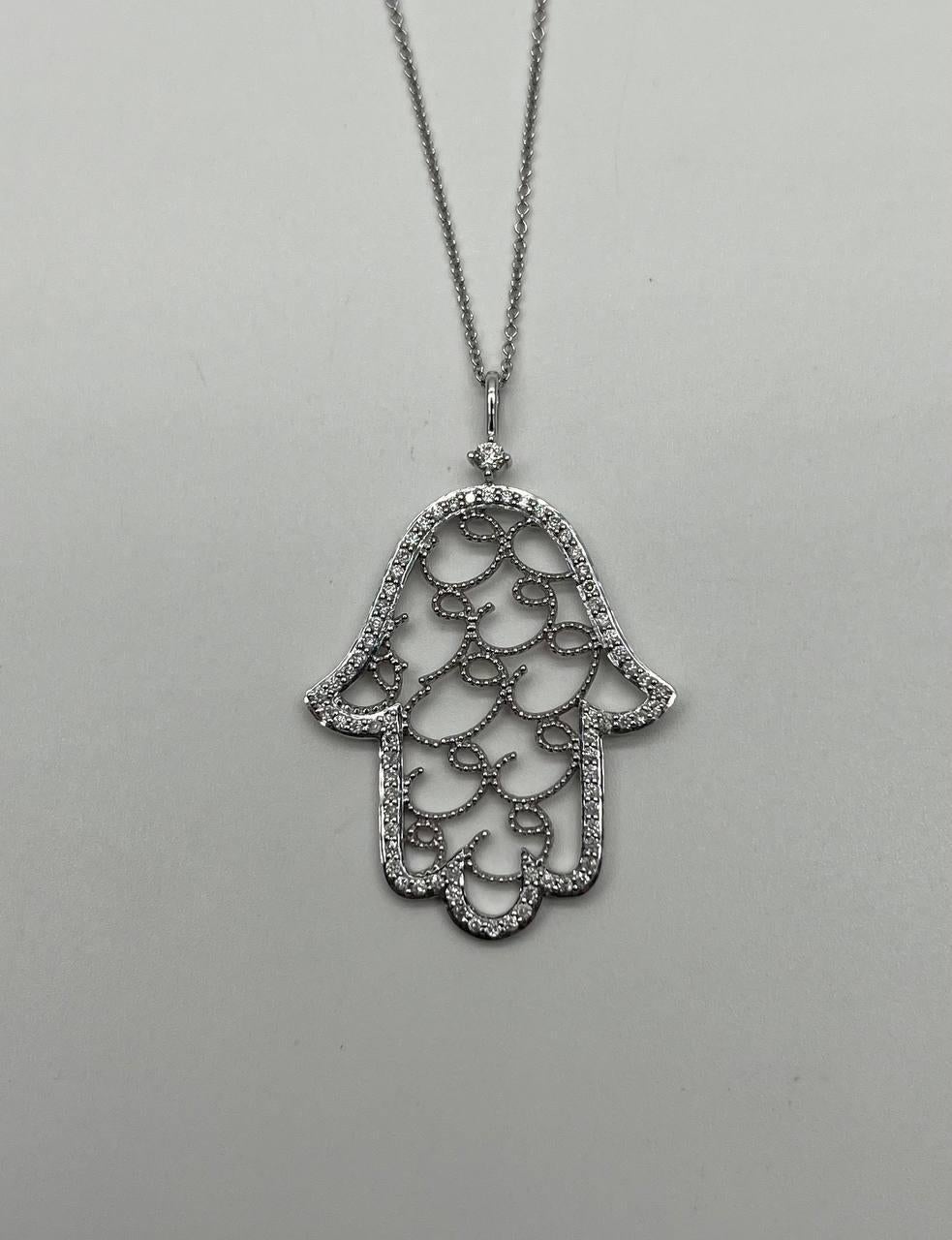 Questo elegante ciondolo presenta un accattivante design traforato. Ornato da scintillanti diamanti bianchi, il pezzo è meticolosamente incastonato in oro bianco 18 carati, creando una miscela armoniosa di scintillio e raffinatezza. Peso totale dei
