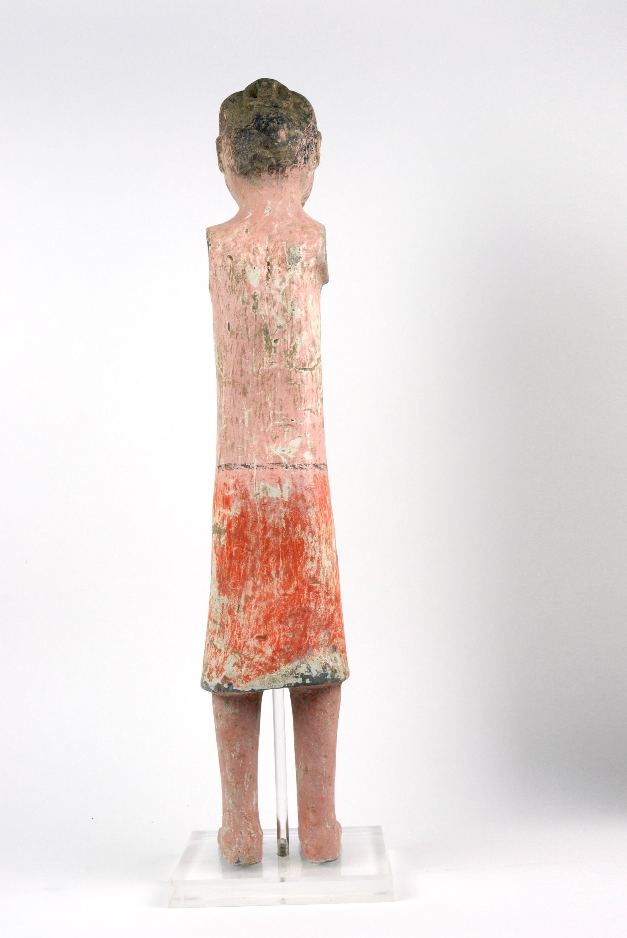 This Han pottery figure of a foot soldier is molded and engraved with facial details. It has been fired at high temperatures. The color pigments are painted on after cooling. This is made of dark pottery and is from Xian. The figure is on a stand