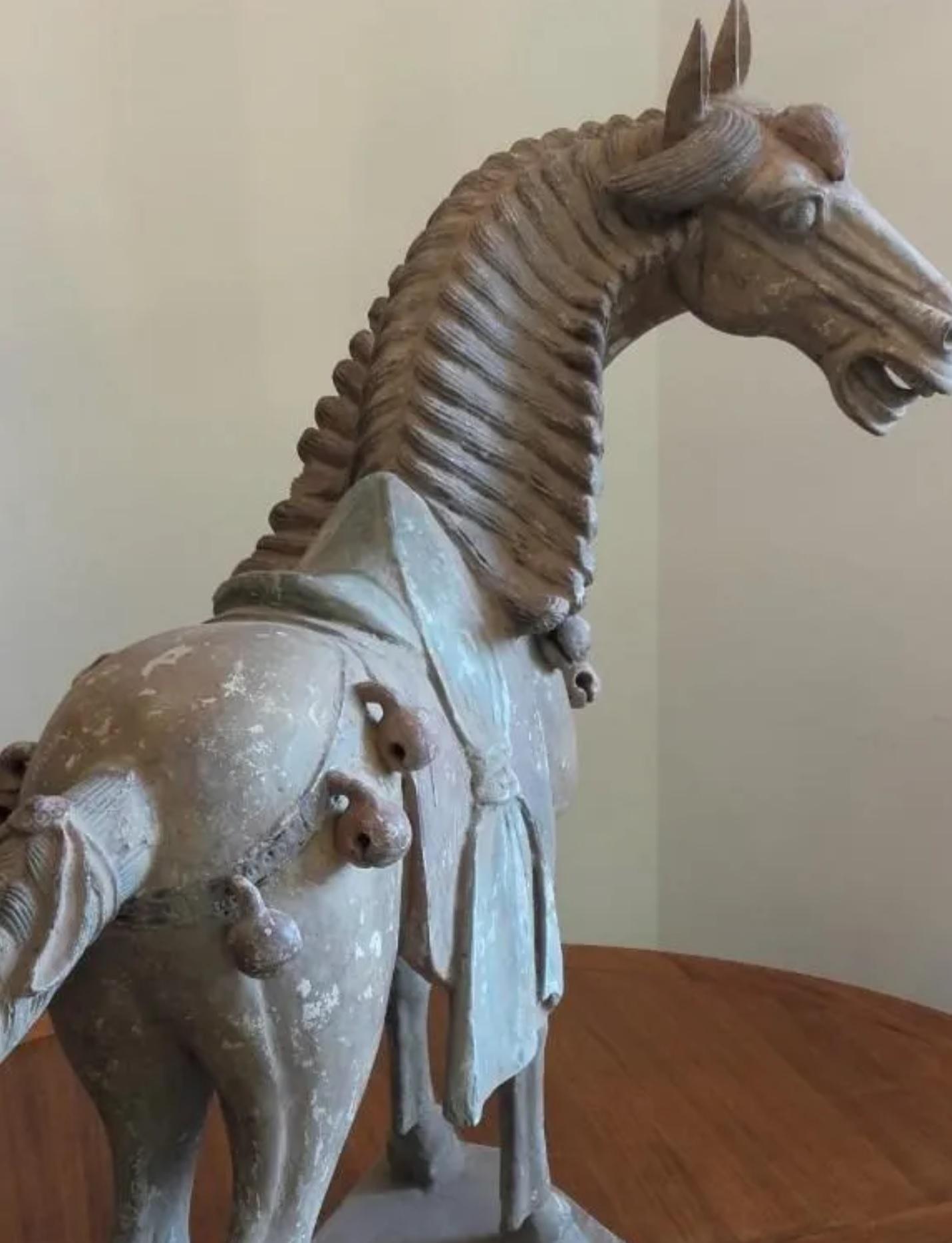 A one piece pottery horse, standing on all fours and striding with its right hoof forward. Extended snout ends in parted lips showing teeth beneath in a braying attitude. Low relief bridle on face and well defined eyes. Raised mane down back of the
