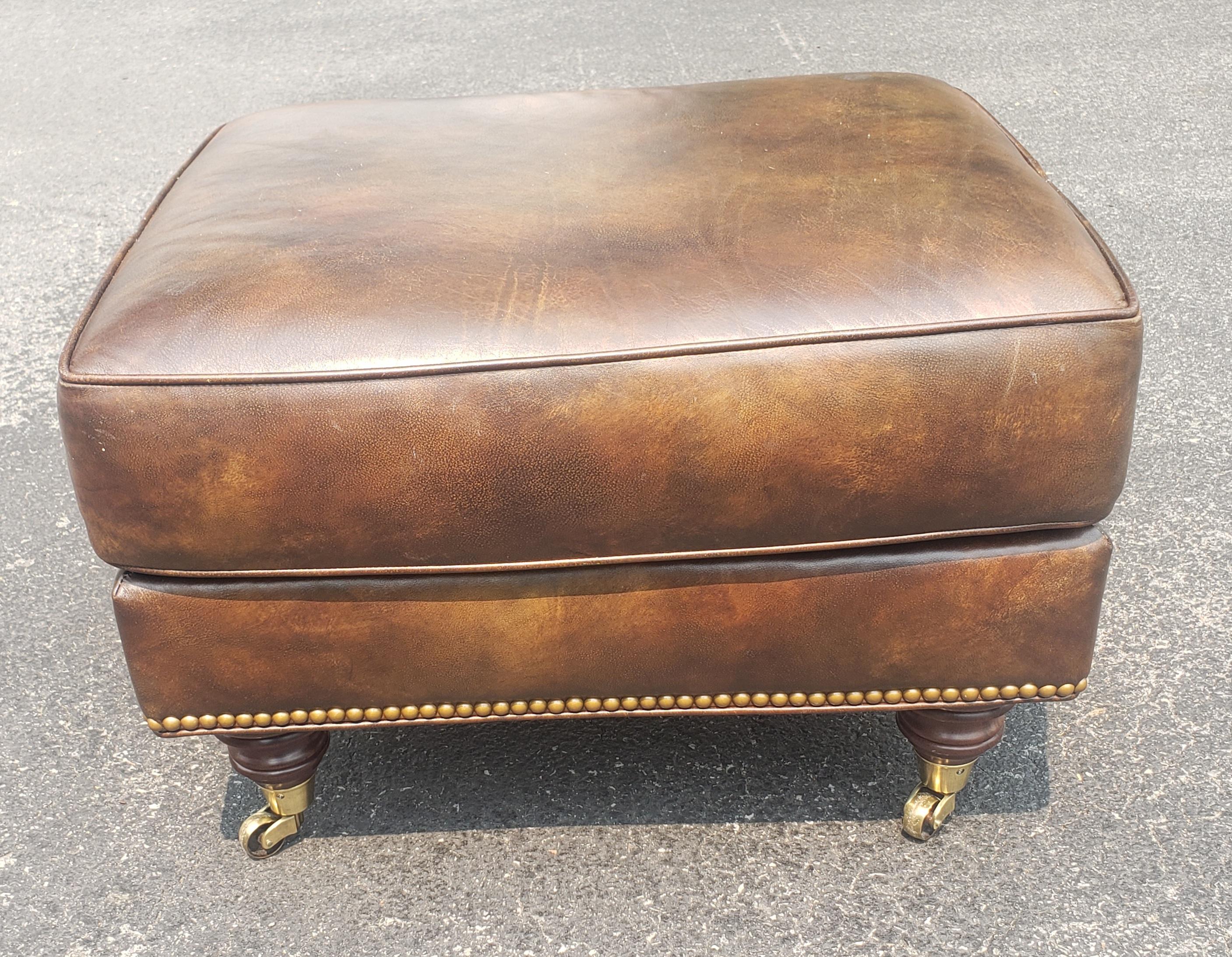 The Bradley Ottoman by Hancock and Moore is a custom made to order full grain leather and brass with nailhead trim and mahogany legs on brass wheels. Distressed look leather by design in excellent condition.