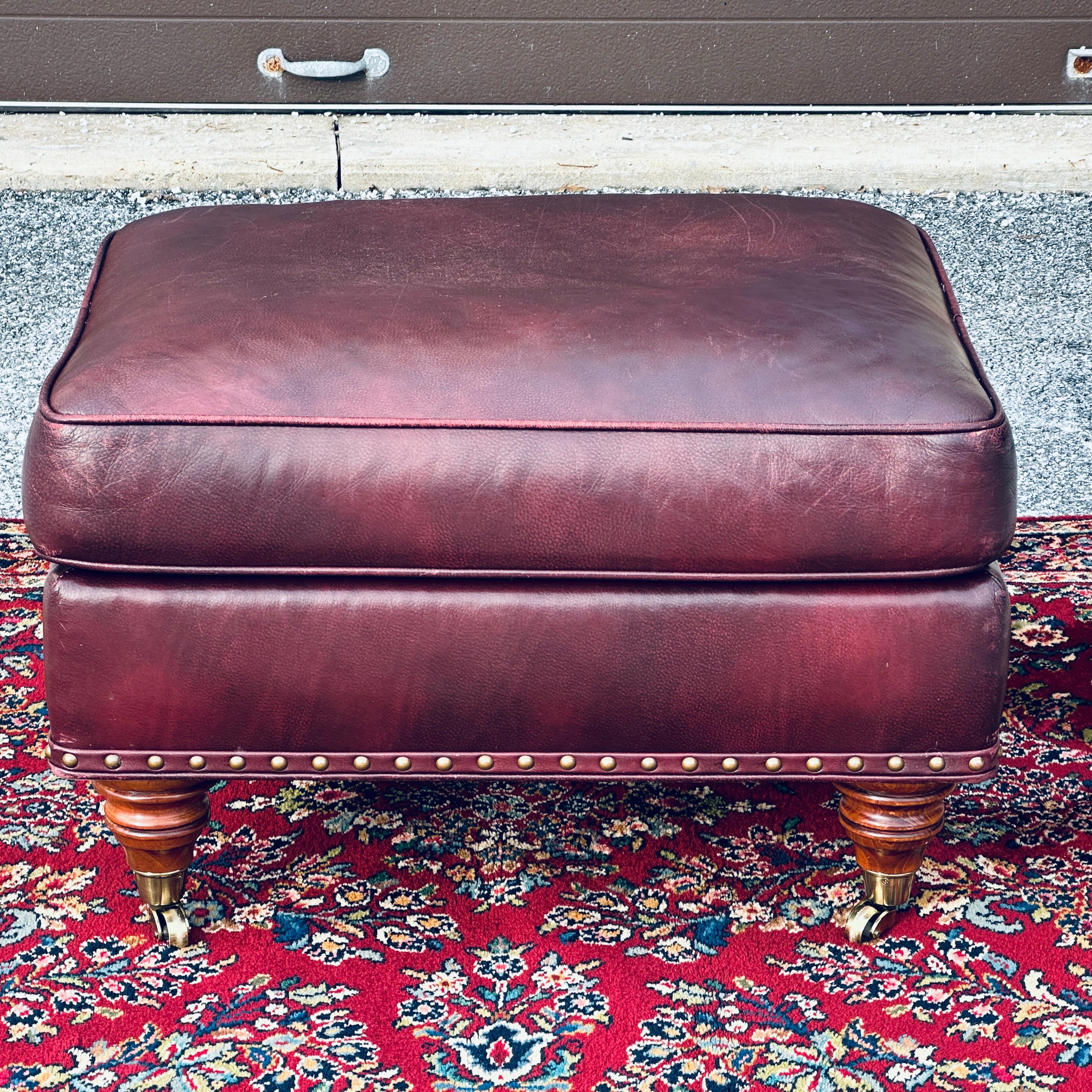 Vintage Hancock & Moore burgundy leather brass nailhead trimmed ottoman on turned wooden legs with brass casters.
