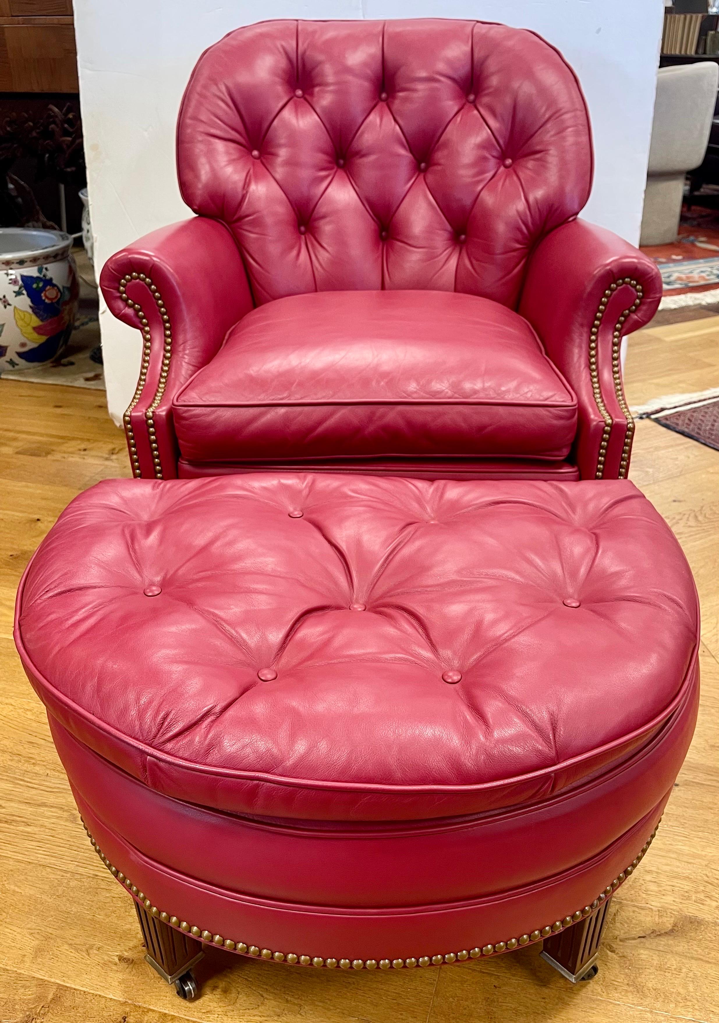 Stunning and coveted Hancock & Moore leather chair and ottoman. The set is labeled underneath. Tufted red raspberry leather with brass tacked detail. Mahogany wood legs with caster wheels for ease of movement. Ottoman in demi-lune shape. Dimensions:
