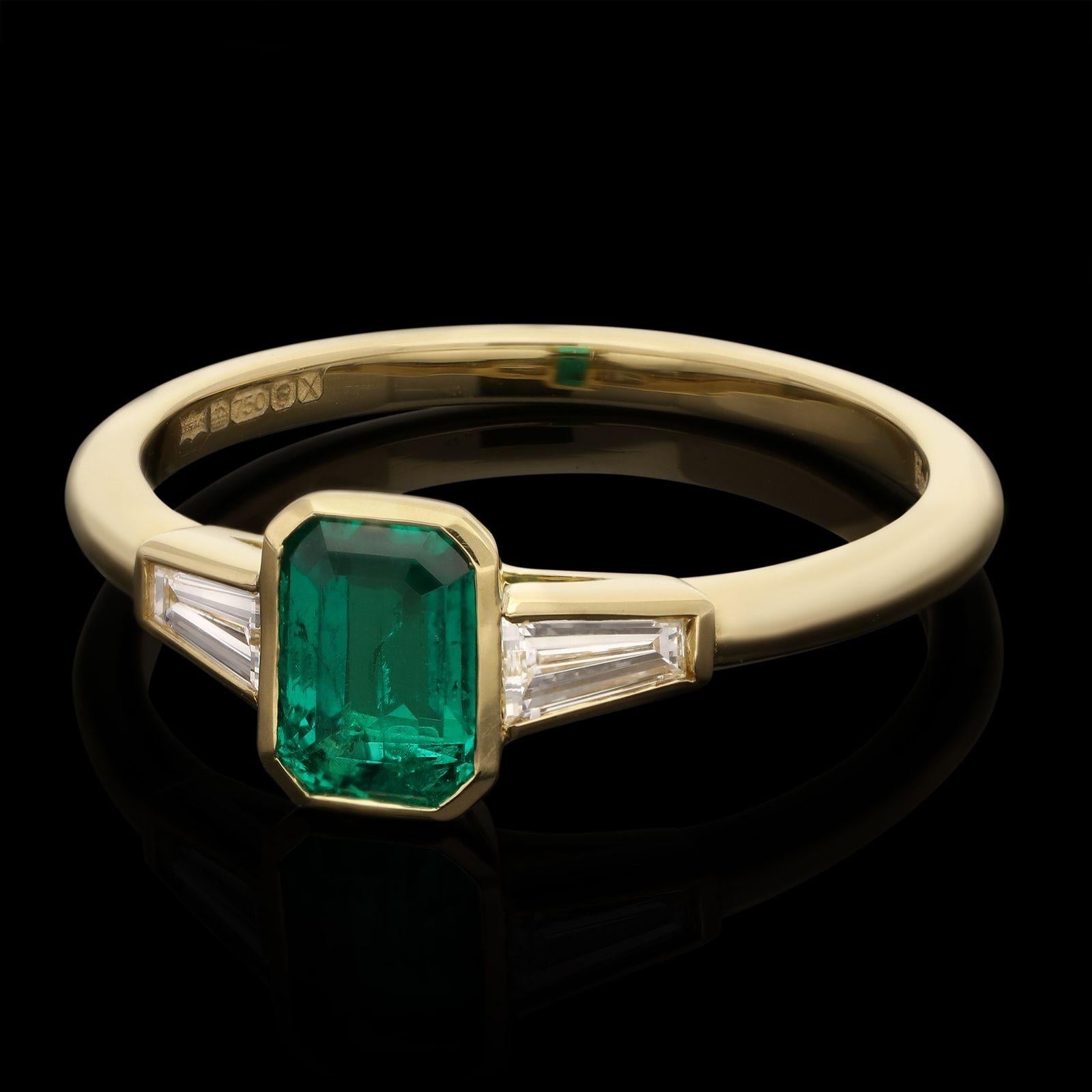 A beautiful emerald and diamond ring by Hancocks, centred on a lovely rich and deeply saturated emerald-cut emerald of Colombian origin weighing 0.68cts rub over set in yellow gold between elegant tapered baguette cut diamond shoulders also in rub
