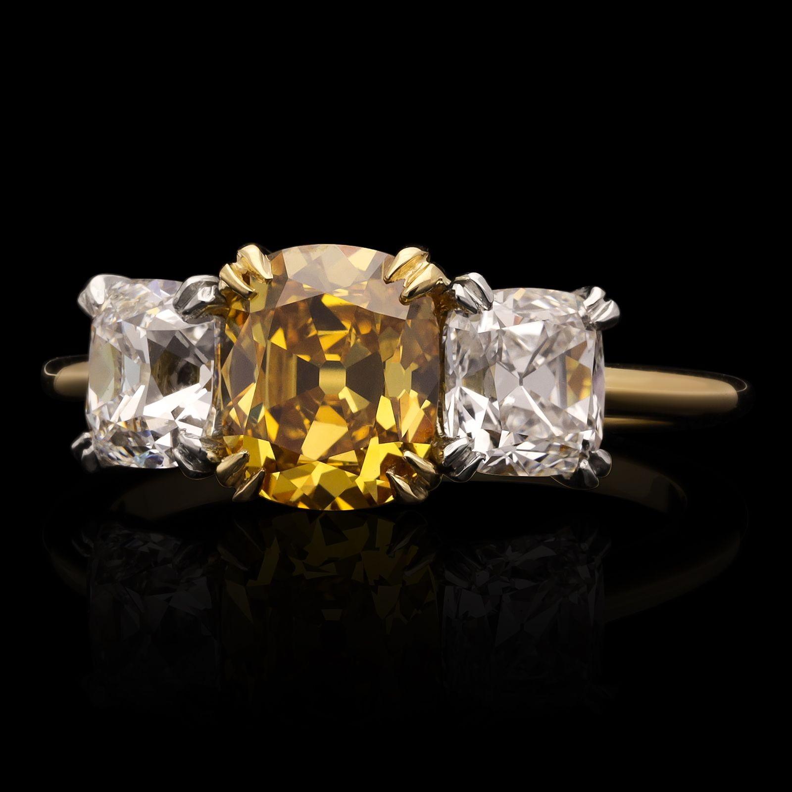 A beautiful old cut fancy coloured diamond and white diamond three stone ring by Hancocks, centred with a wonderful old mine brilliant cut diamond weighing 1.42cts and of Fancy Deep Orange Yellow colour and VS2 clarity, claw set in 18ct yellow gold