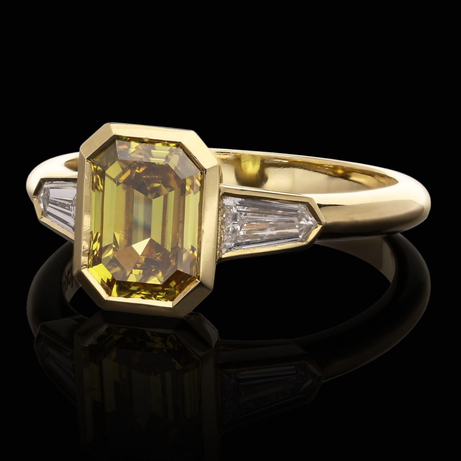 A beautiful fancy yellow diamond and white diamond ring by Hancocks, the ring centred on an emerald-cut diamond weighing 1.52ct and of fancy deep yellow colour and SI1 clarity, rub over set in 18ct yellow gold between shoulders set with tapered