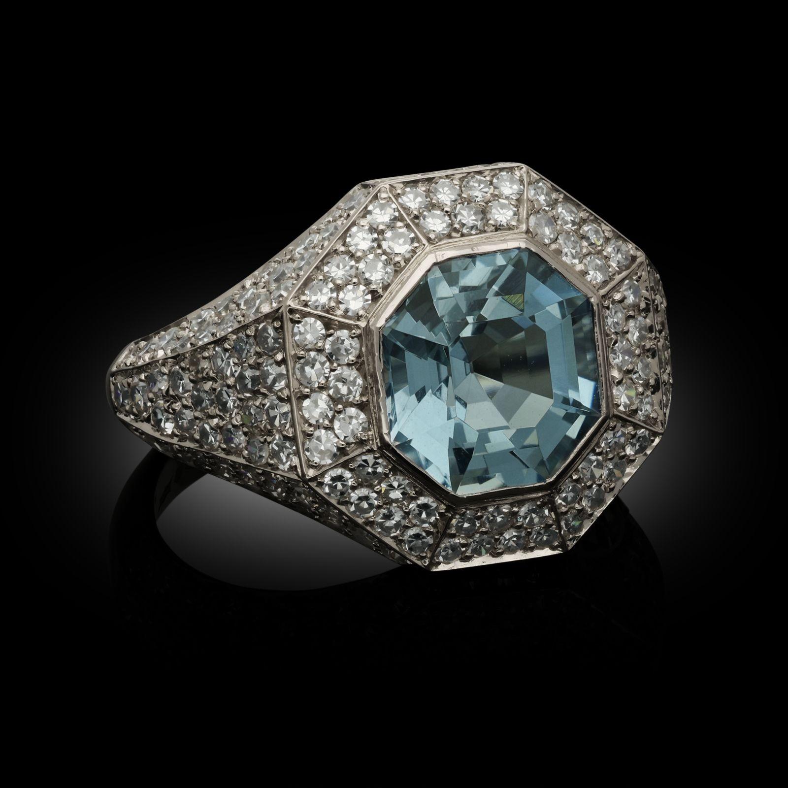 A beautiful geometric aquamarine and diamond ring by Hancocks, centred with an octagonal step-cut aquamarine weighing 2.02cts in rubover setting surrounded by a double row of single cut diamonds in an angled halo frame, all in a hand crafted